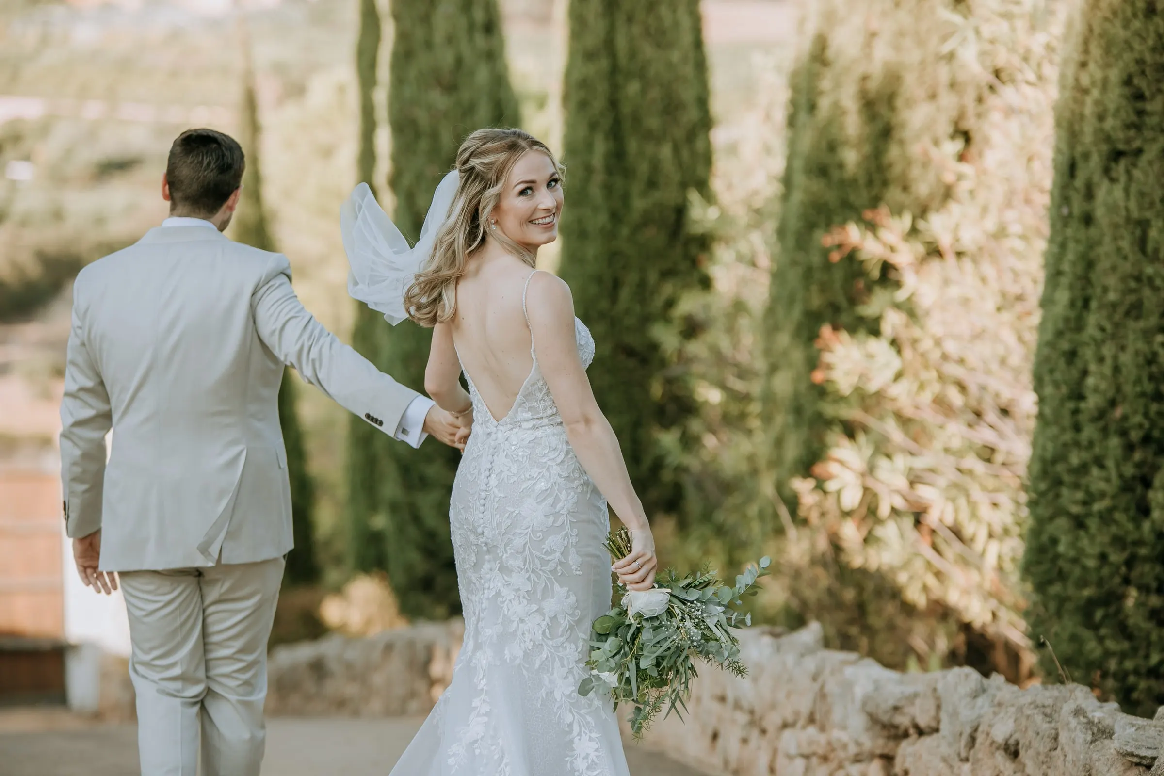 Bride looking back over her shoulder as the groom leads her past the cypresses, Hacienda San José, Mijas
