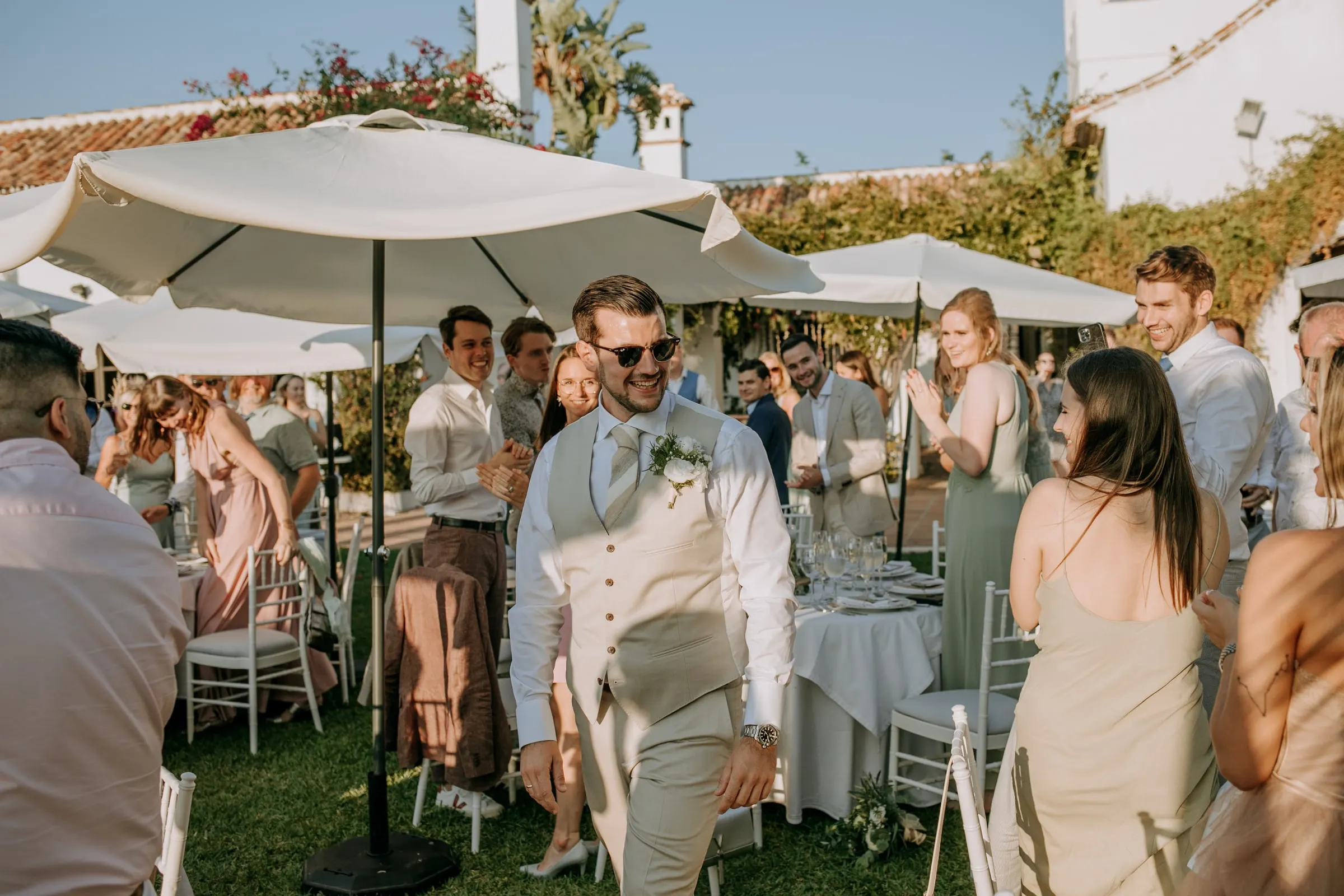 Groom in sunglasses and waistcoat walking through guests at the garden drinks, Hacienda San José, Mijas