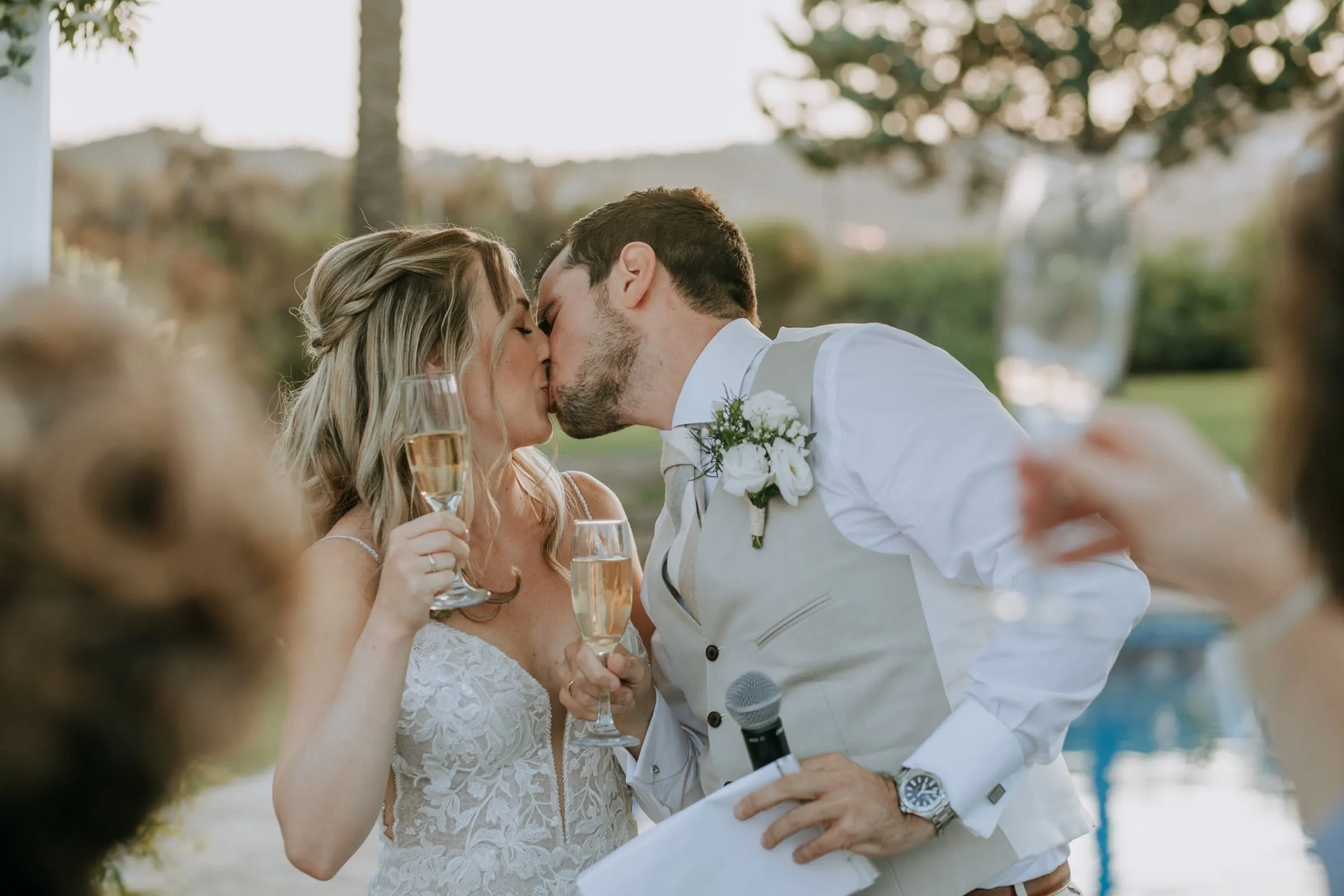 Bride and groom kiss mid-toast, glasses of cava in hand, as guests raise theirs, Hacienda San José, Mijas