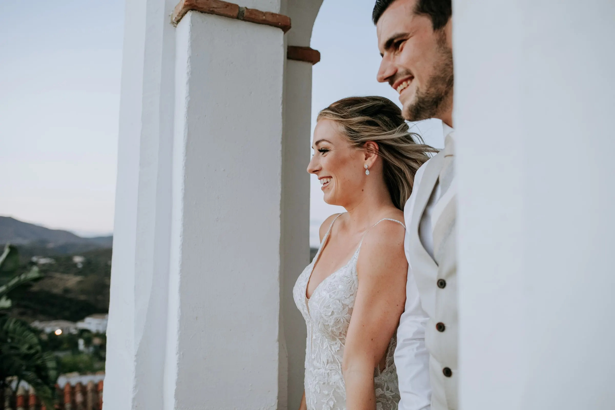 Bride and groom smiling side by side on a white terrace at dusk, hills behind, Hacienda San José, Mijas