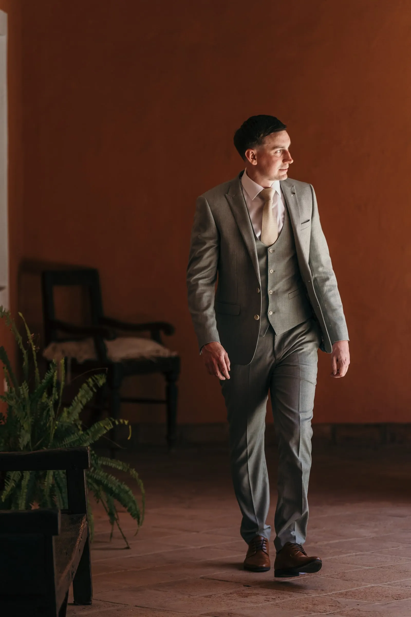 Groom in a three-piece grey suit walking across a terracotta room