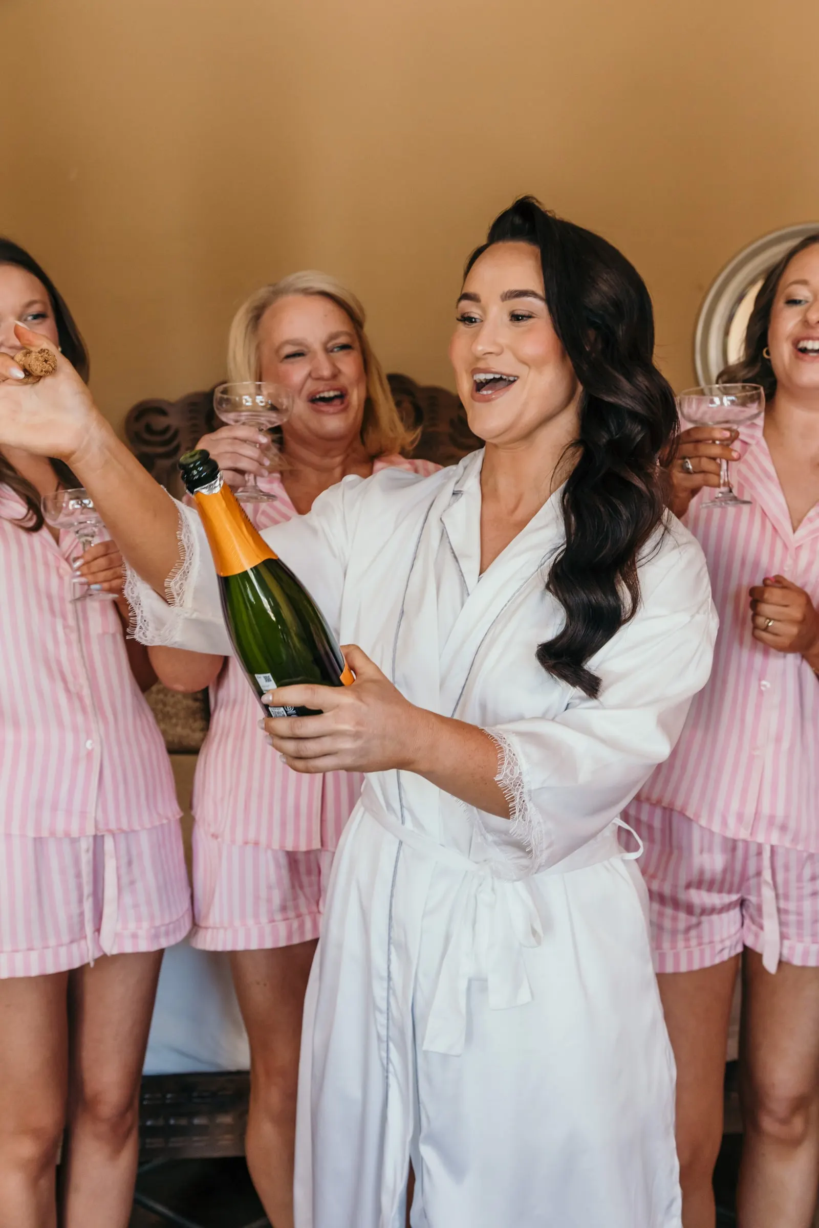 Bride popping champagne among bridesmaids in pink striped pyjamas