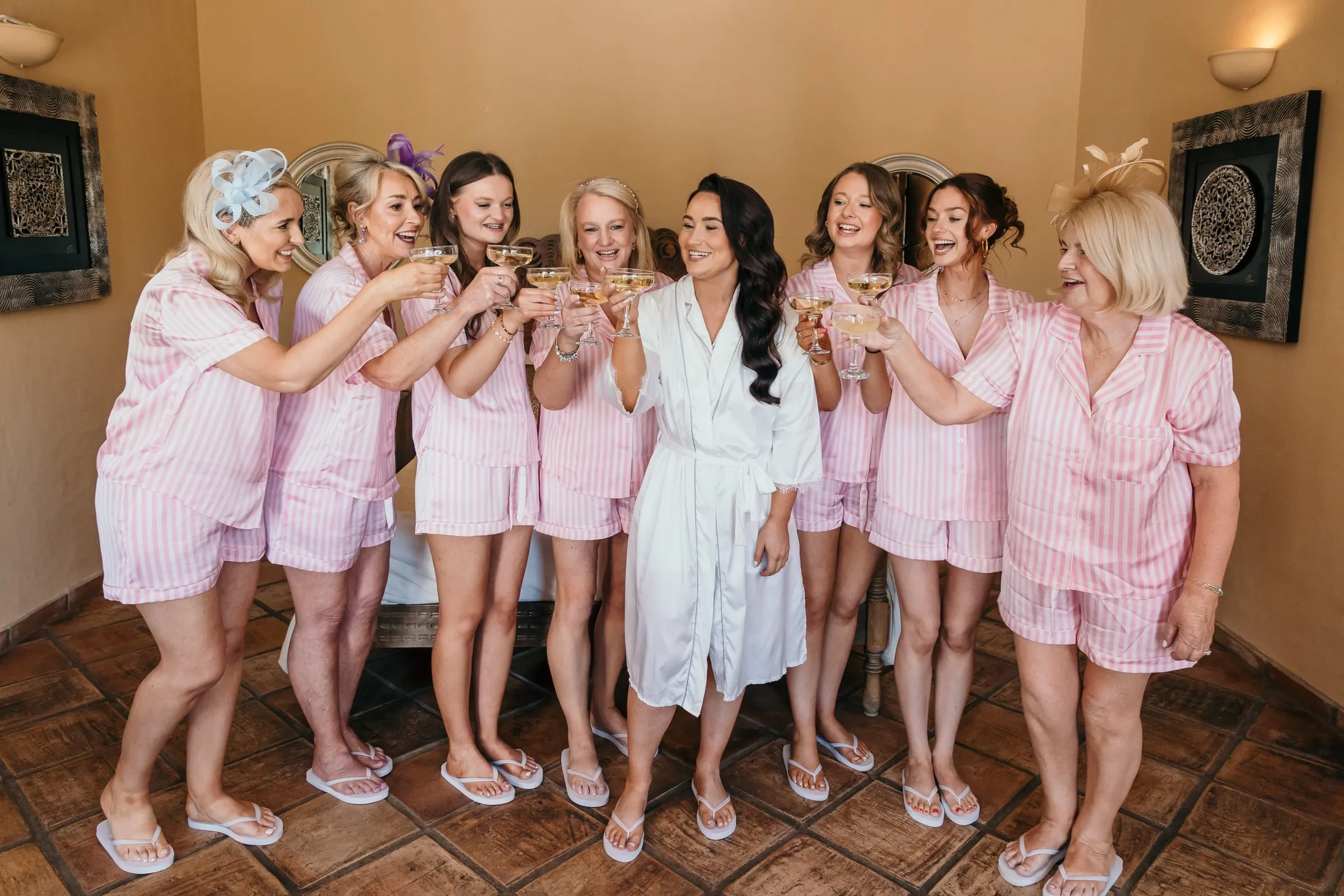 Bride and bridesmaids in pink pyjamas toasting with coupes, Hacienda San José