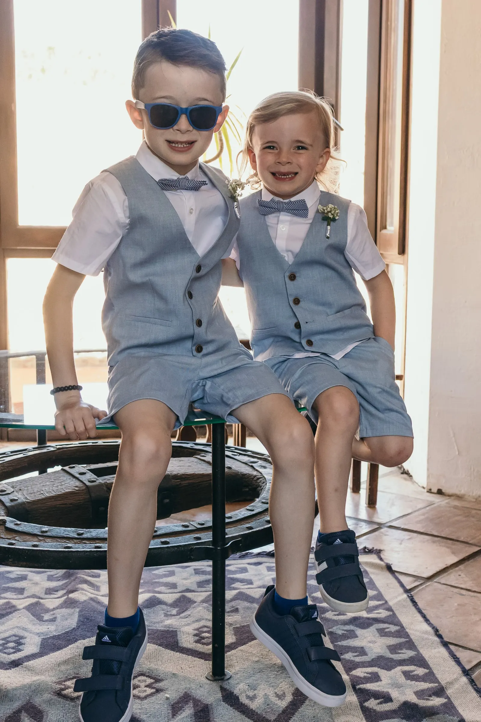 Two page boys in grey waistcoats and sunglasses sitting on a stool