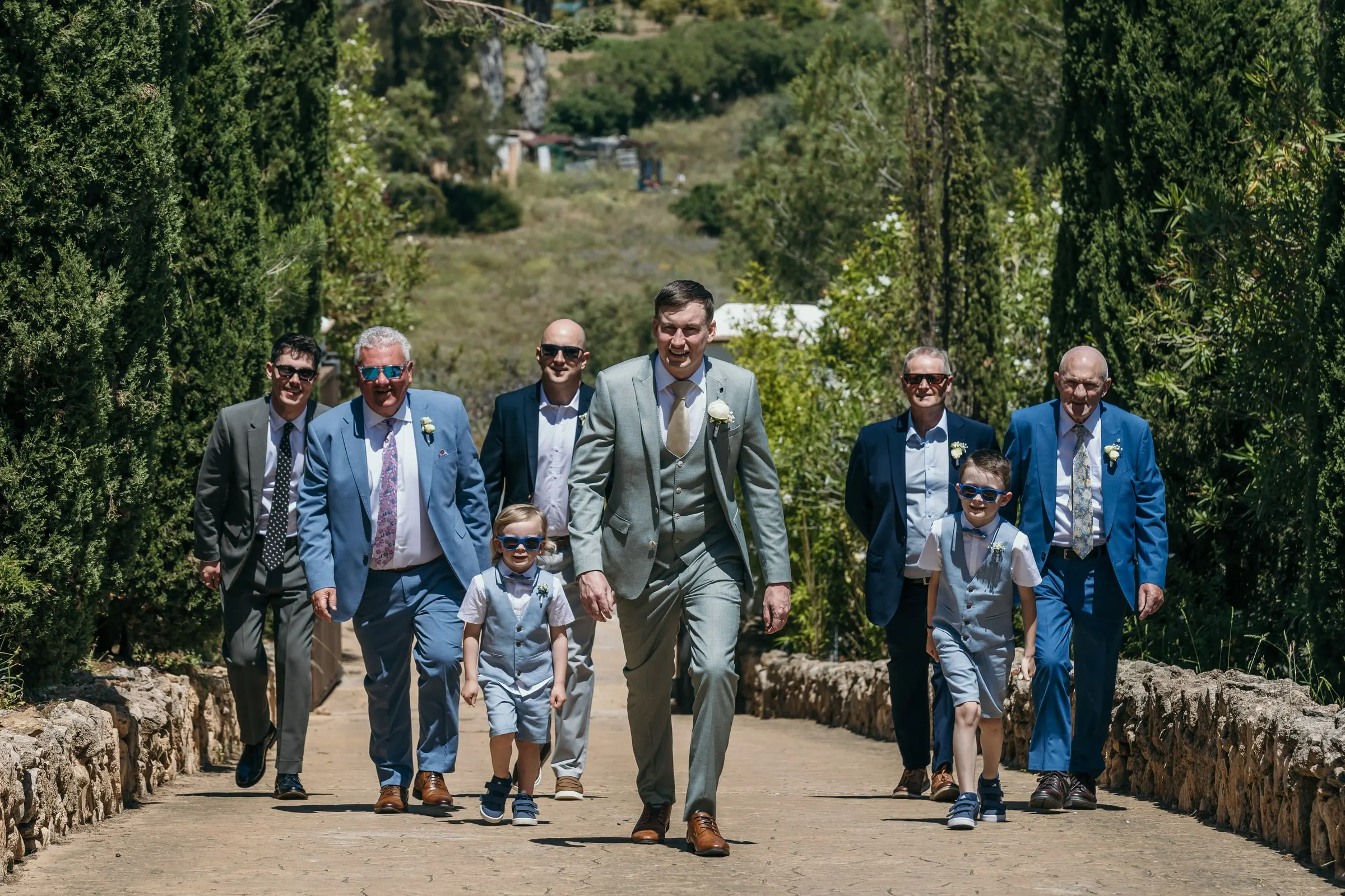 Groom and friends walking down the stone-walled drive, Hacienda San José, Mijas
