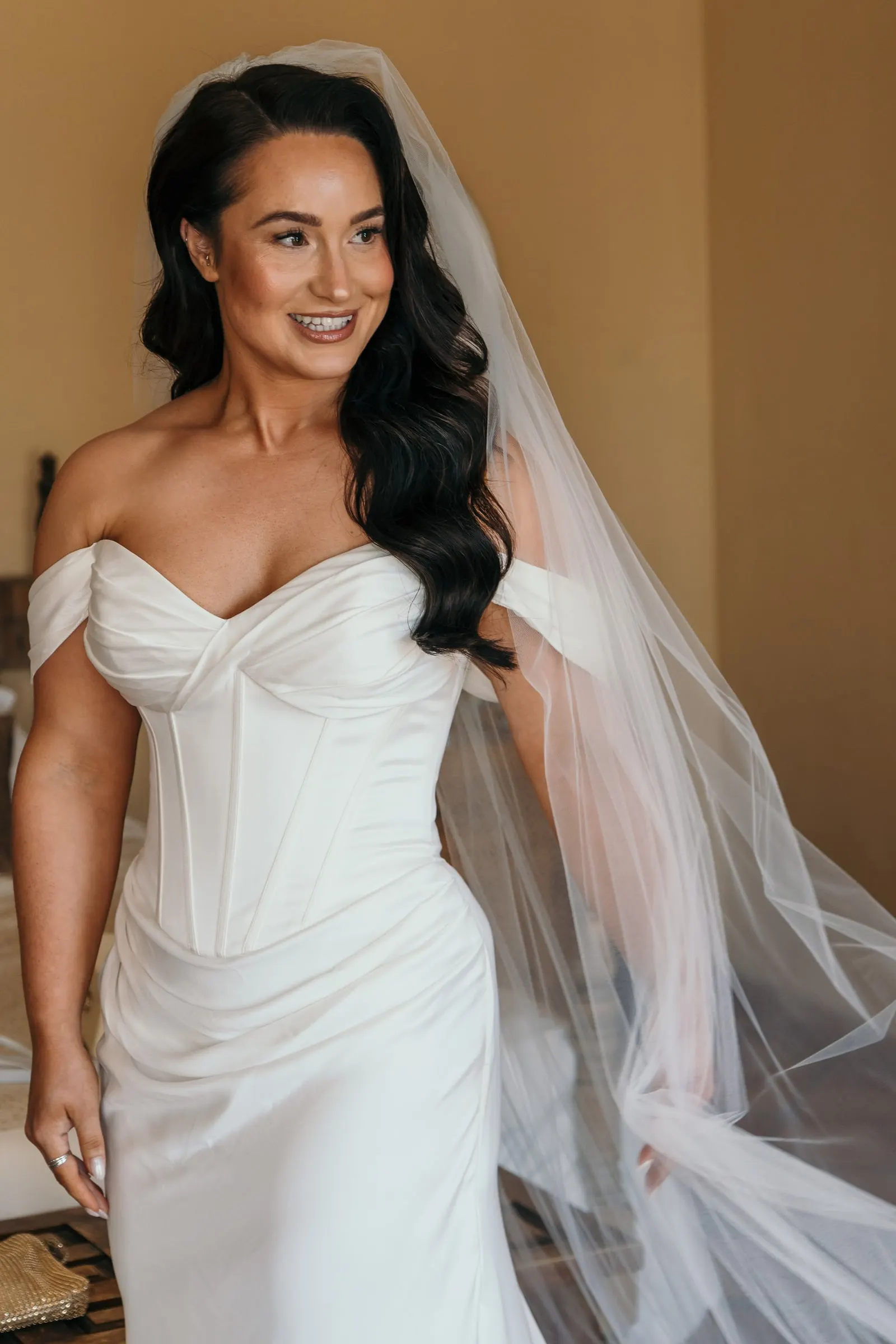 Bride in her corset gown and long veil smiling in a sunny room