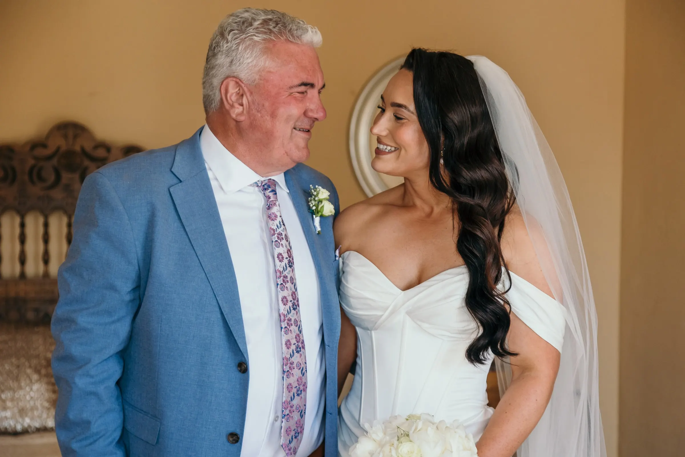 Bride sharing a smile with a man in a blue suit before the ceremony