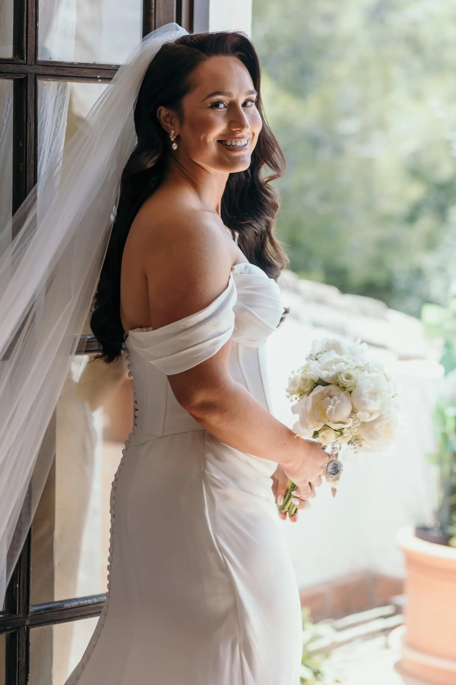 Bride with her bouquet of white roses looking back over her shoulder in a doorway