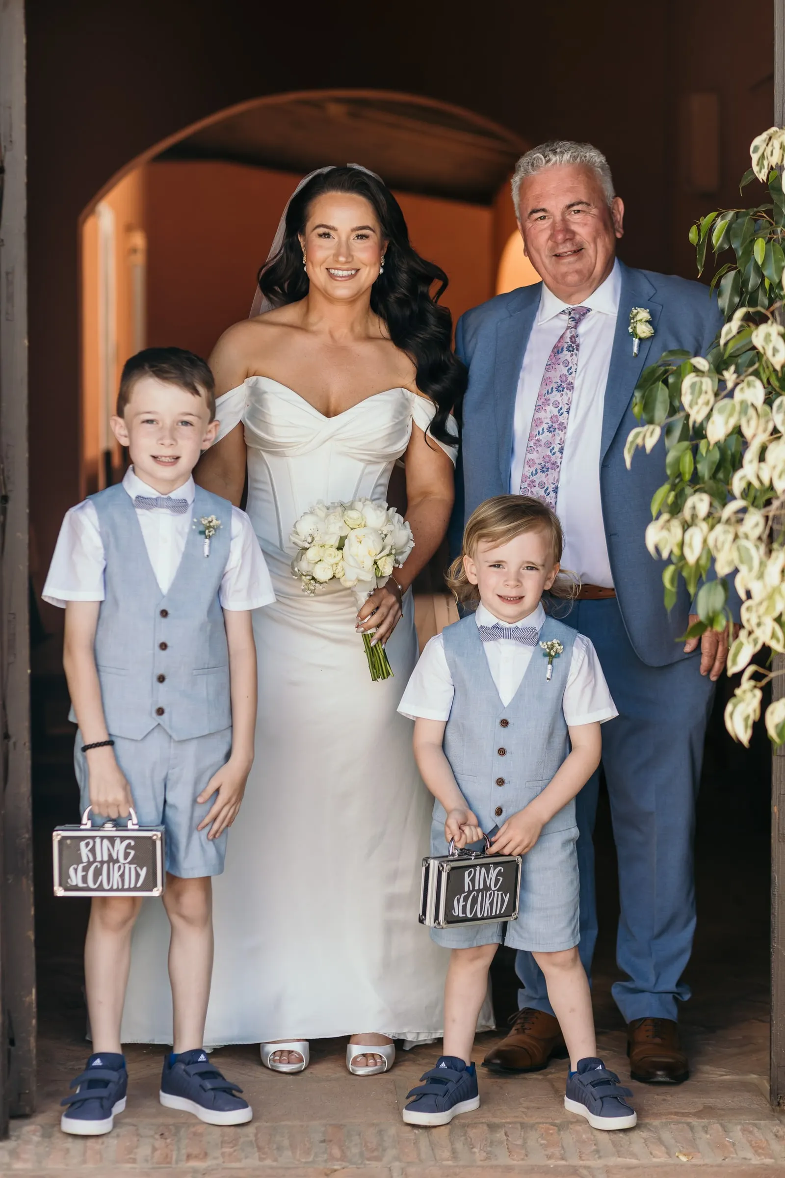 Bride with two page boys holding Ring Security signs under an arch