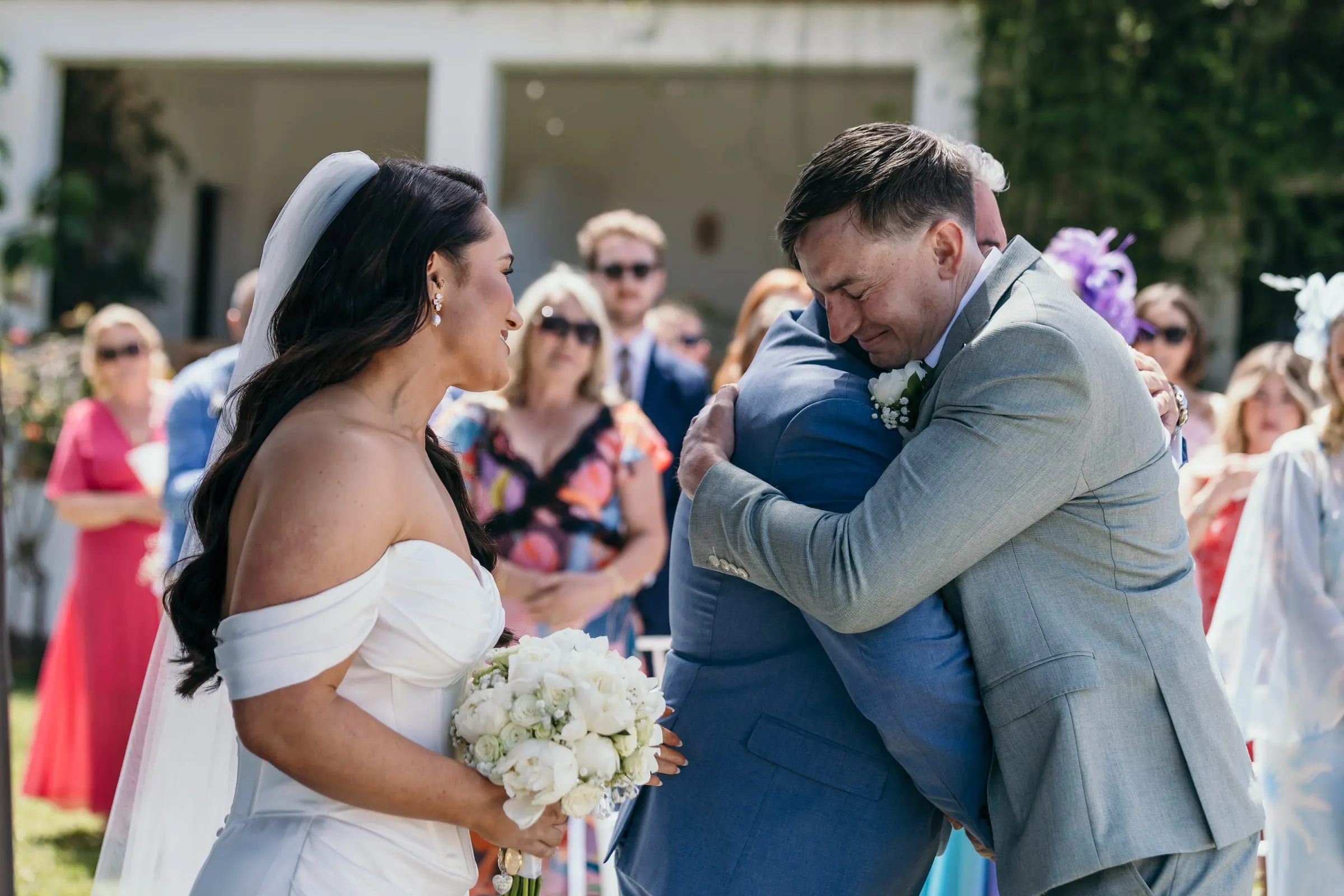 Groom hugging a man in a blue suit at the end of the aisle