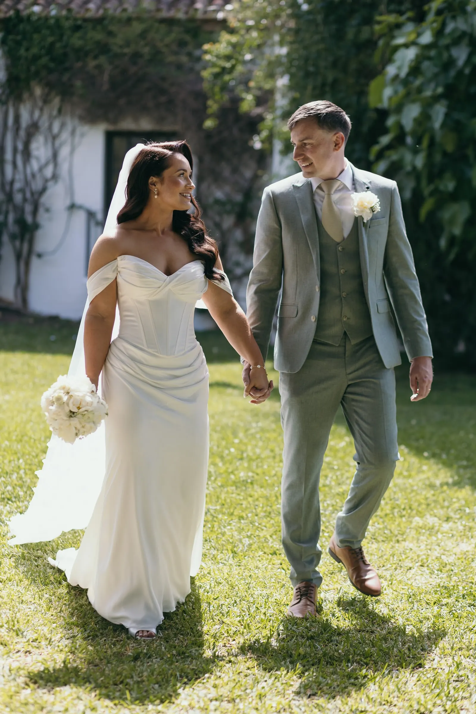 Bride and groom walking hand in hand across the lawn