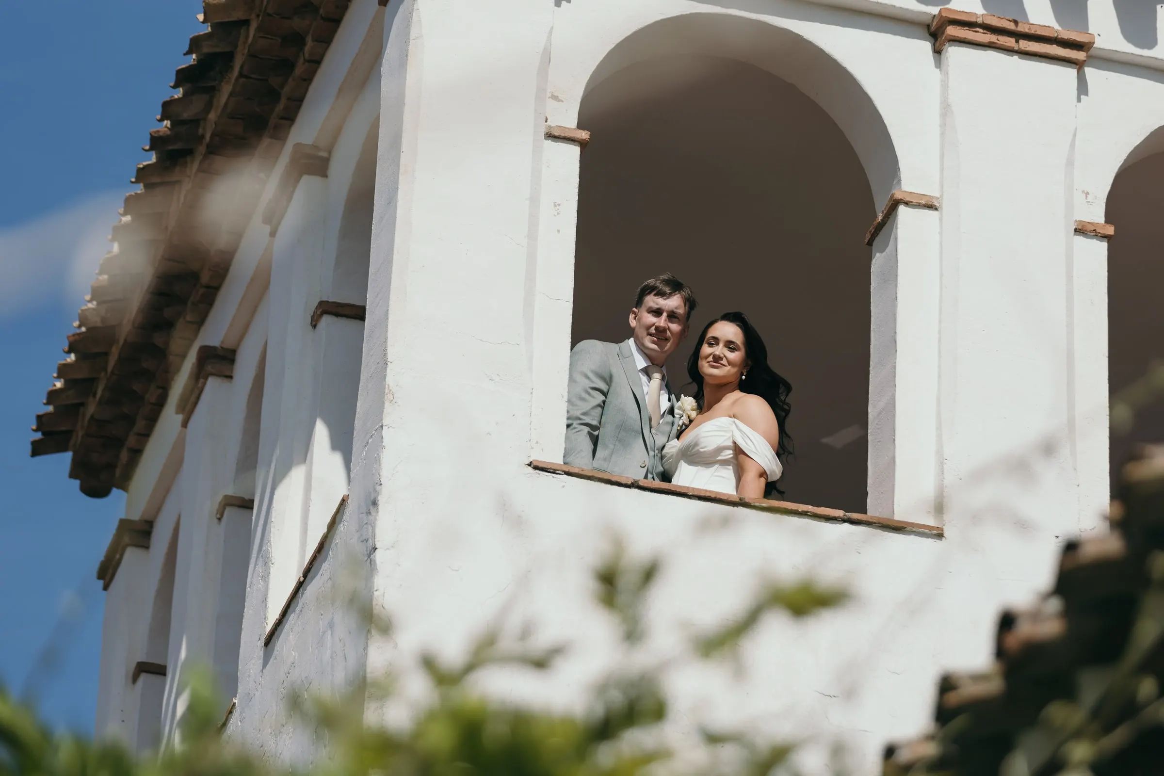 Bride and groom smiling down from the arches of the tower