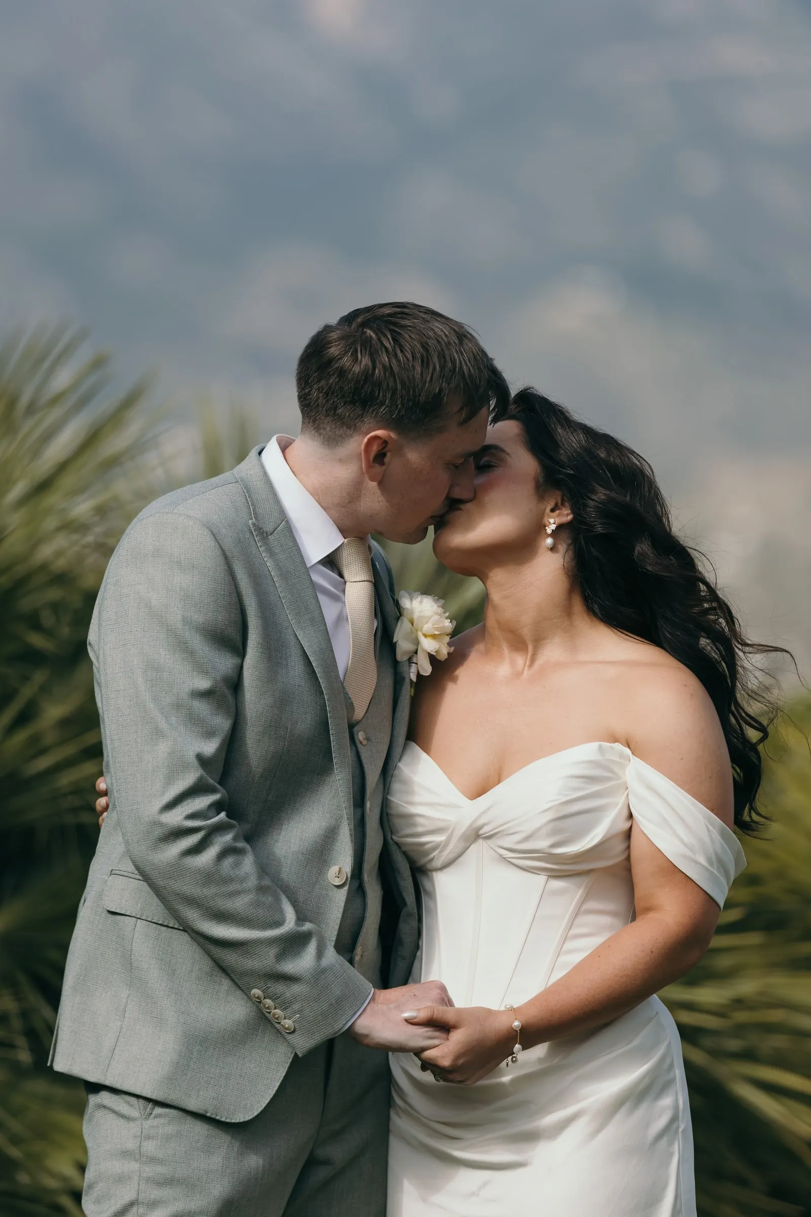 Couple kissing among palm leaves with the mountains in soft focus