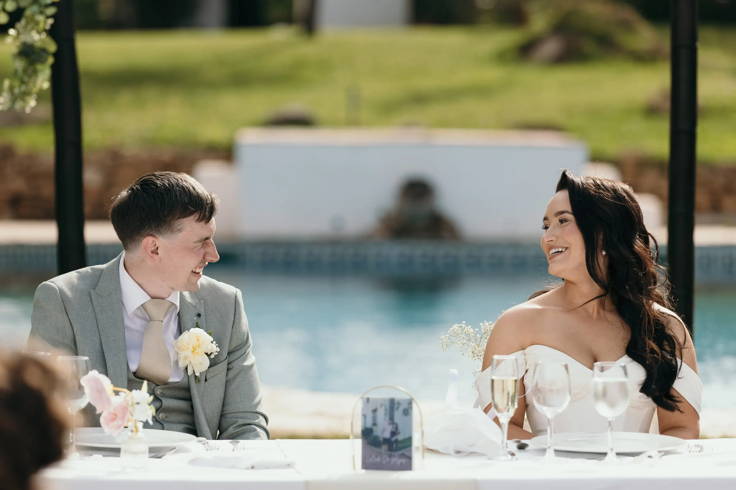 Bride and groom laughing at the top table with the pool behind them, Mijas