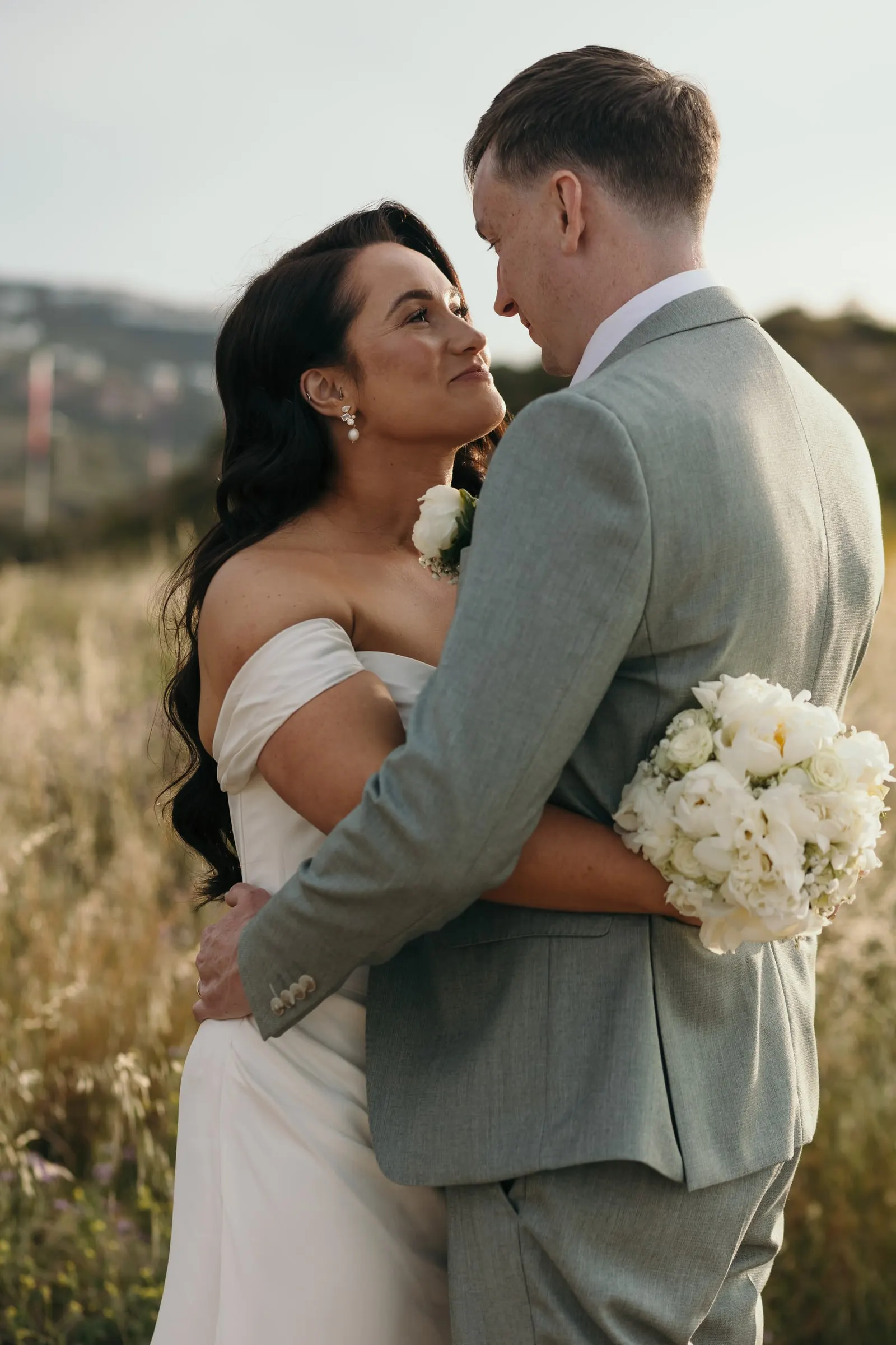 Bride hugging the groom with her bouquet of white roses in the long grass