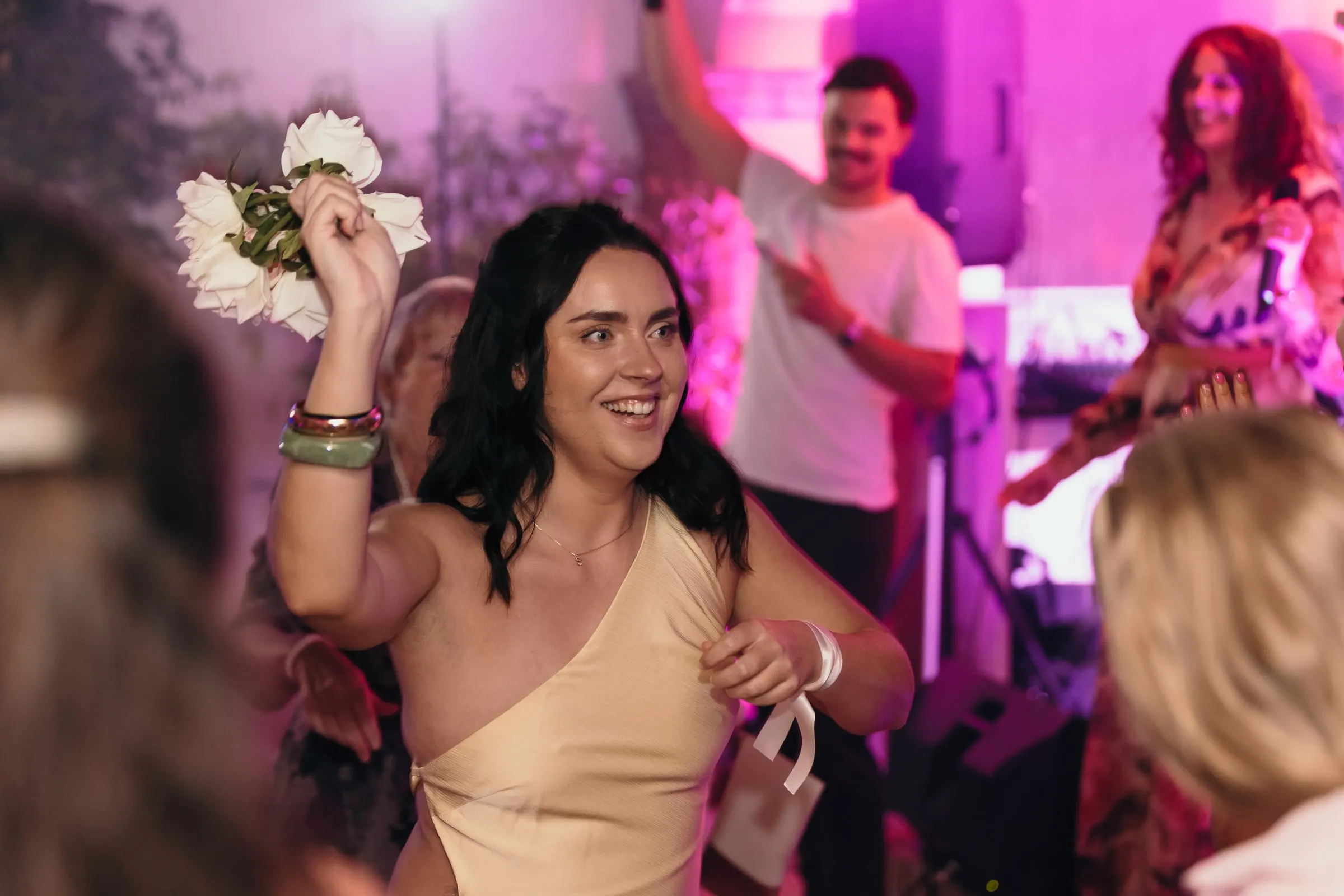 Guest waving the bride's bouquet on the dance floor under pink light