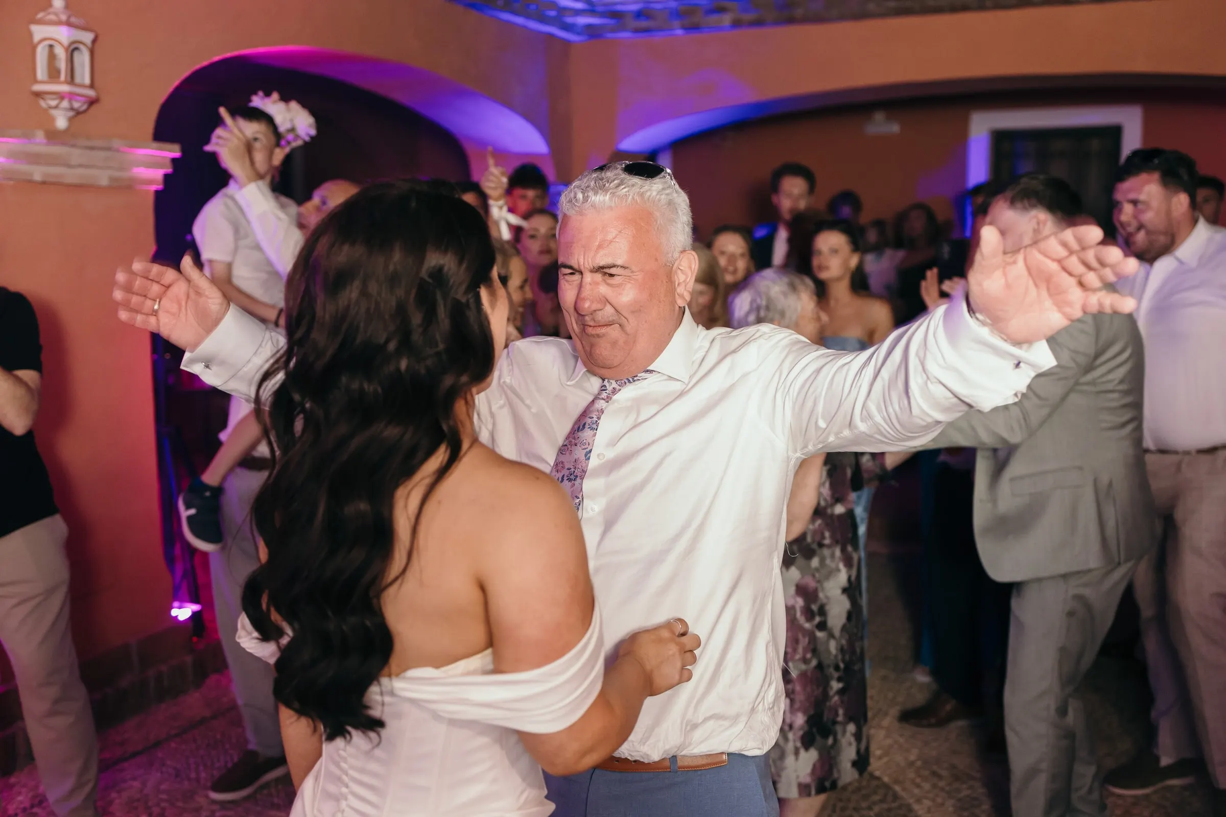 Man in a white shirt dancing with his arms wide in front of the bride