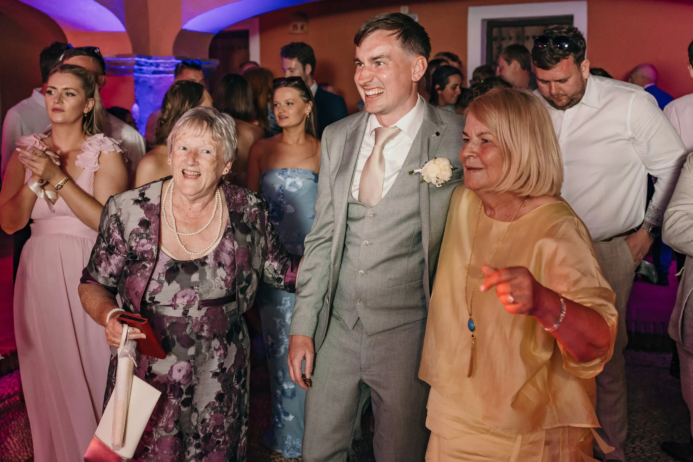 Groom laughing between two guests on the dance floor