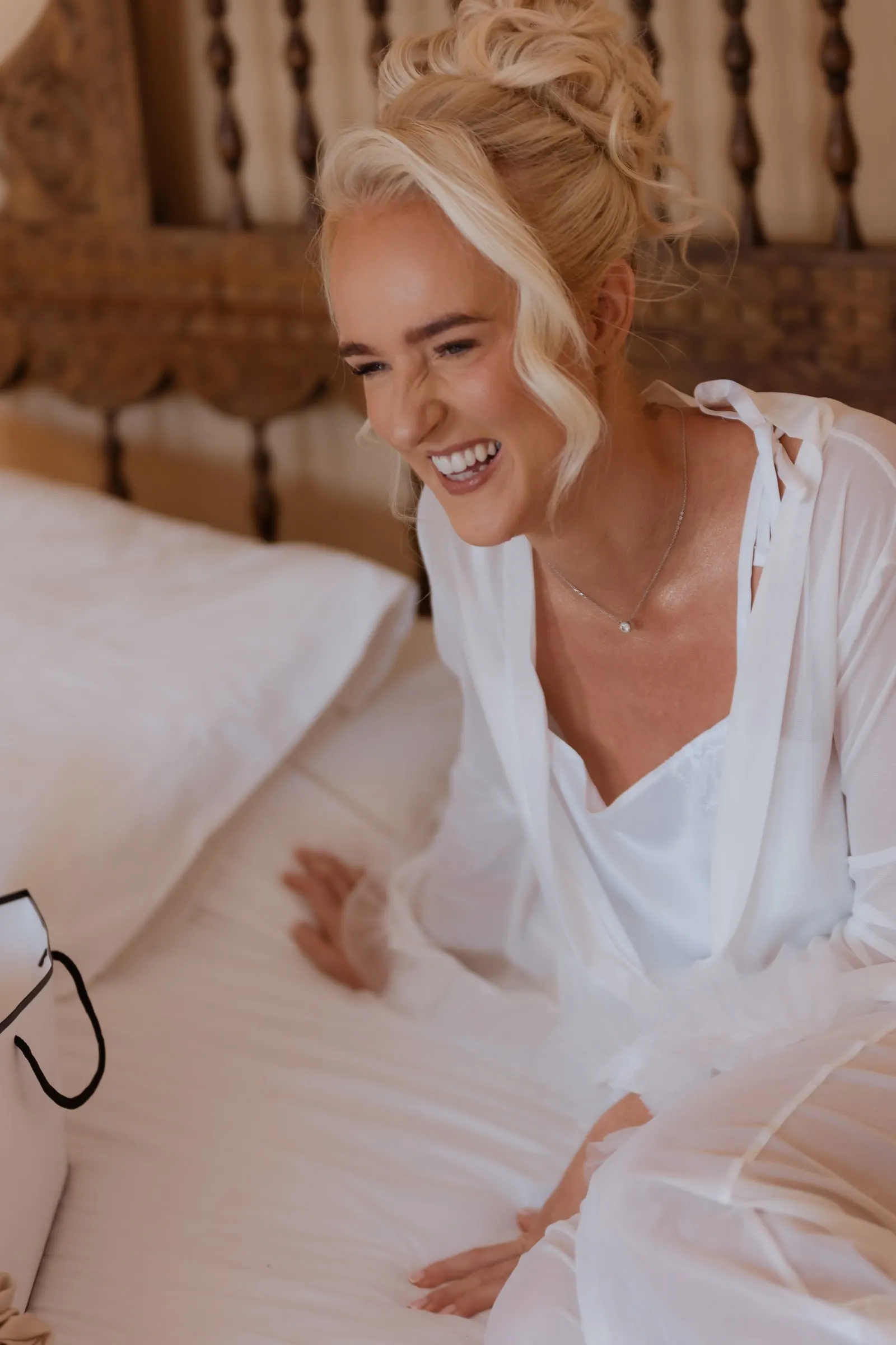 Bride laughing on the bed in a white robe in the bridal suite at Hacienda San José