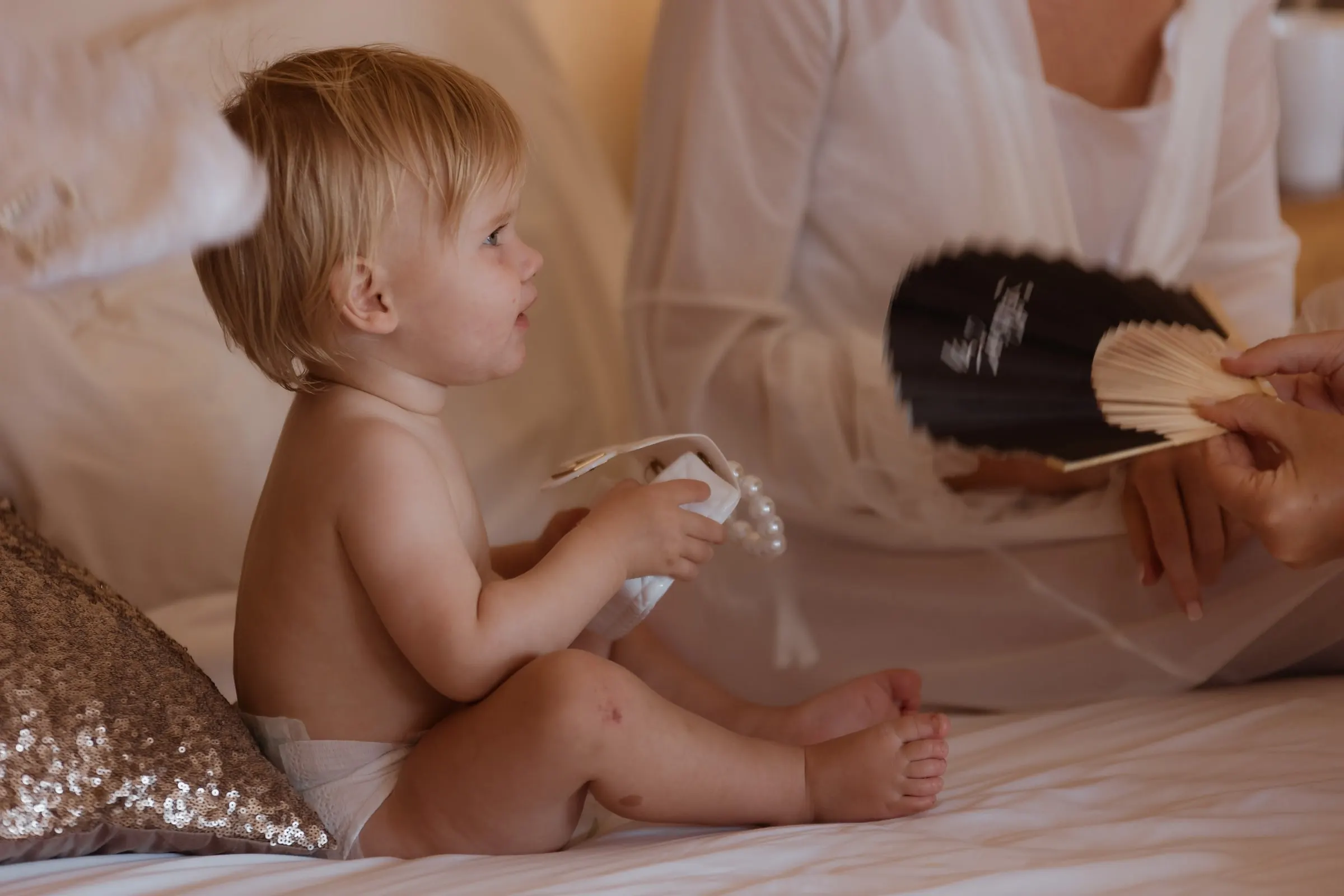 Baby sitting on the bed playing with a fan in the bridal suite