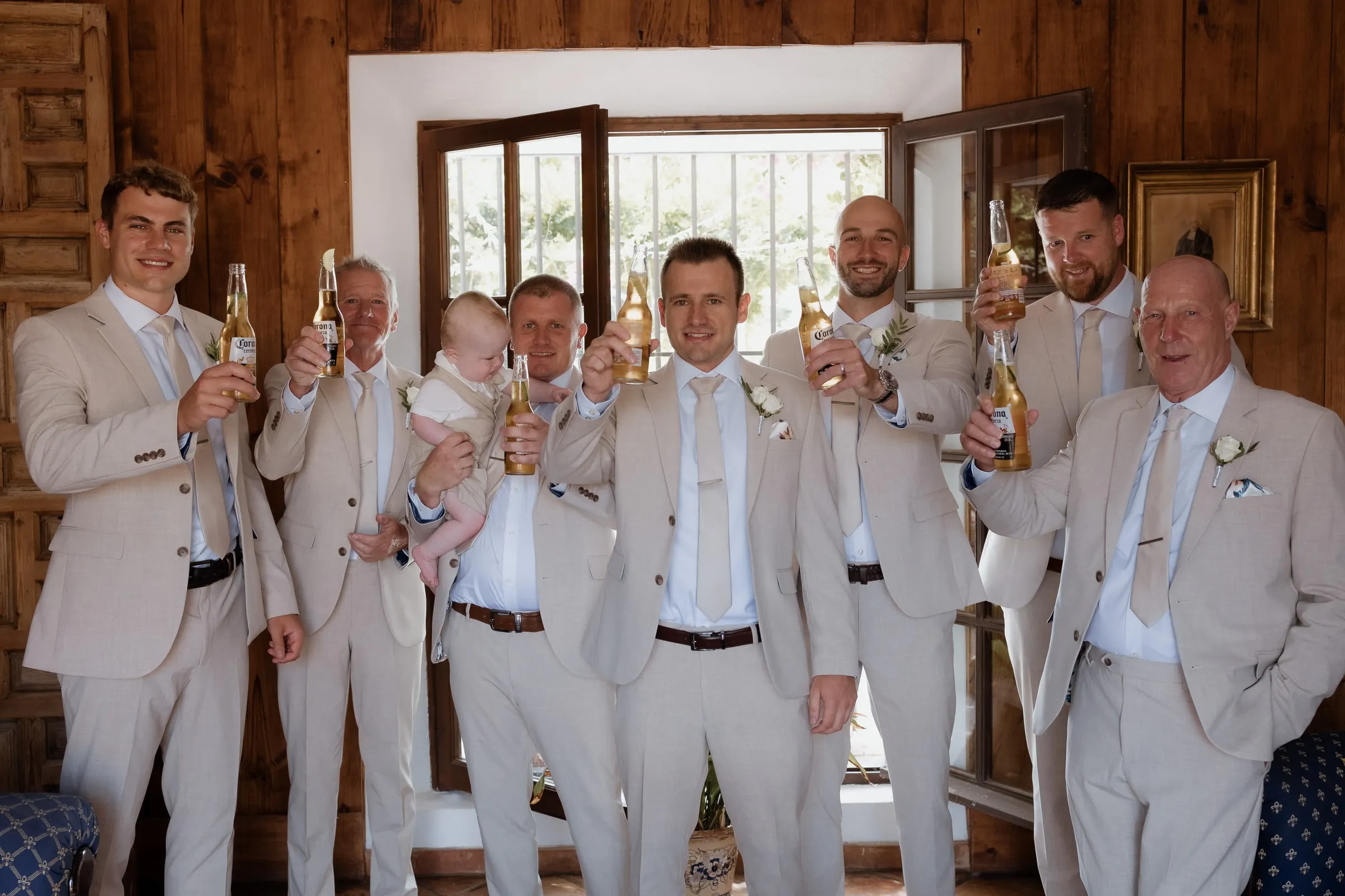 Groom and groomsmen in beige suits raising a toast in a wood-panelled room in Mijas