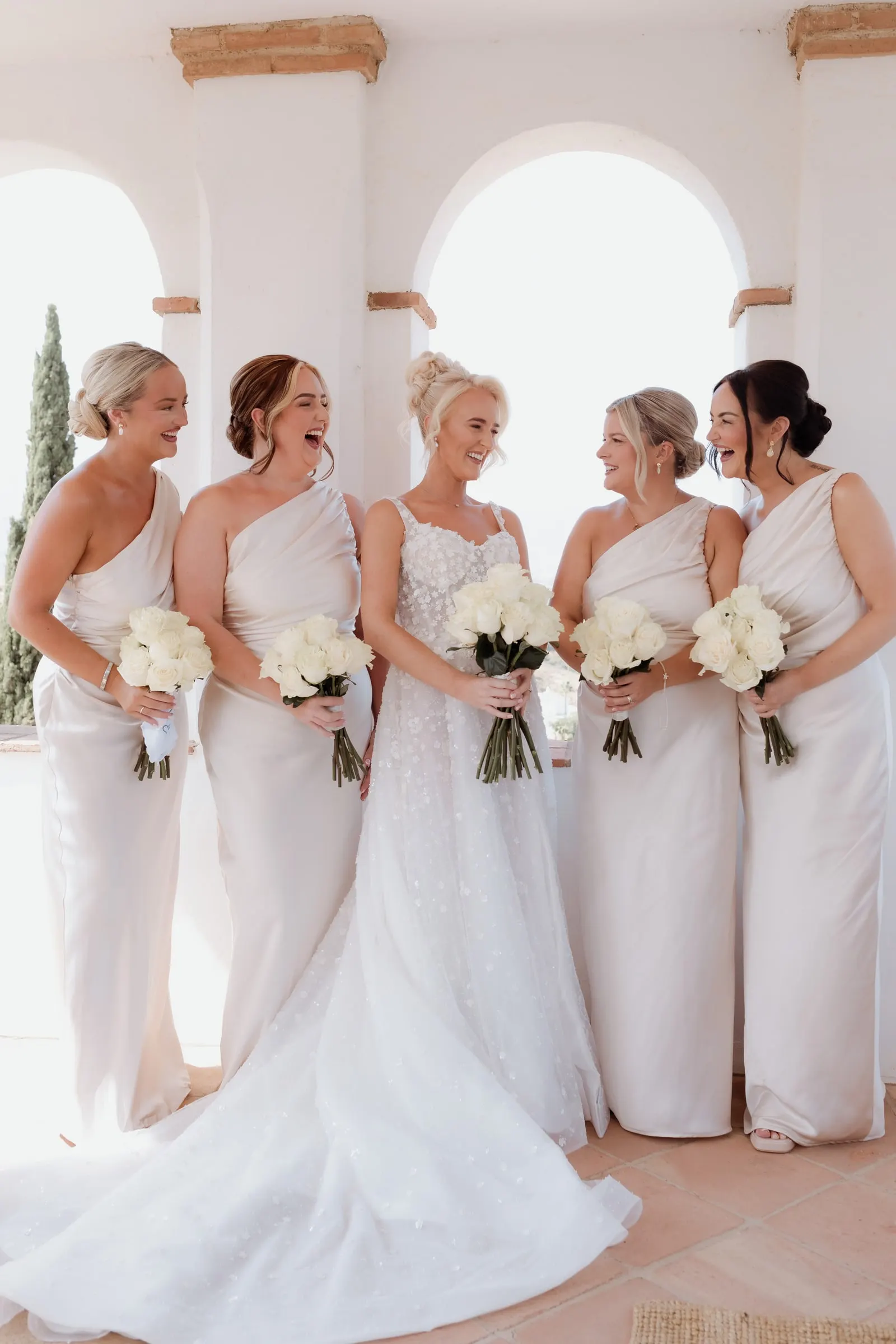 Bride and bridesmaids with white rose bouquets in the arched loggia at Hacienda San José
