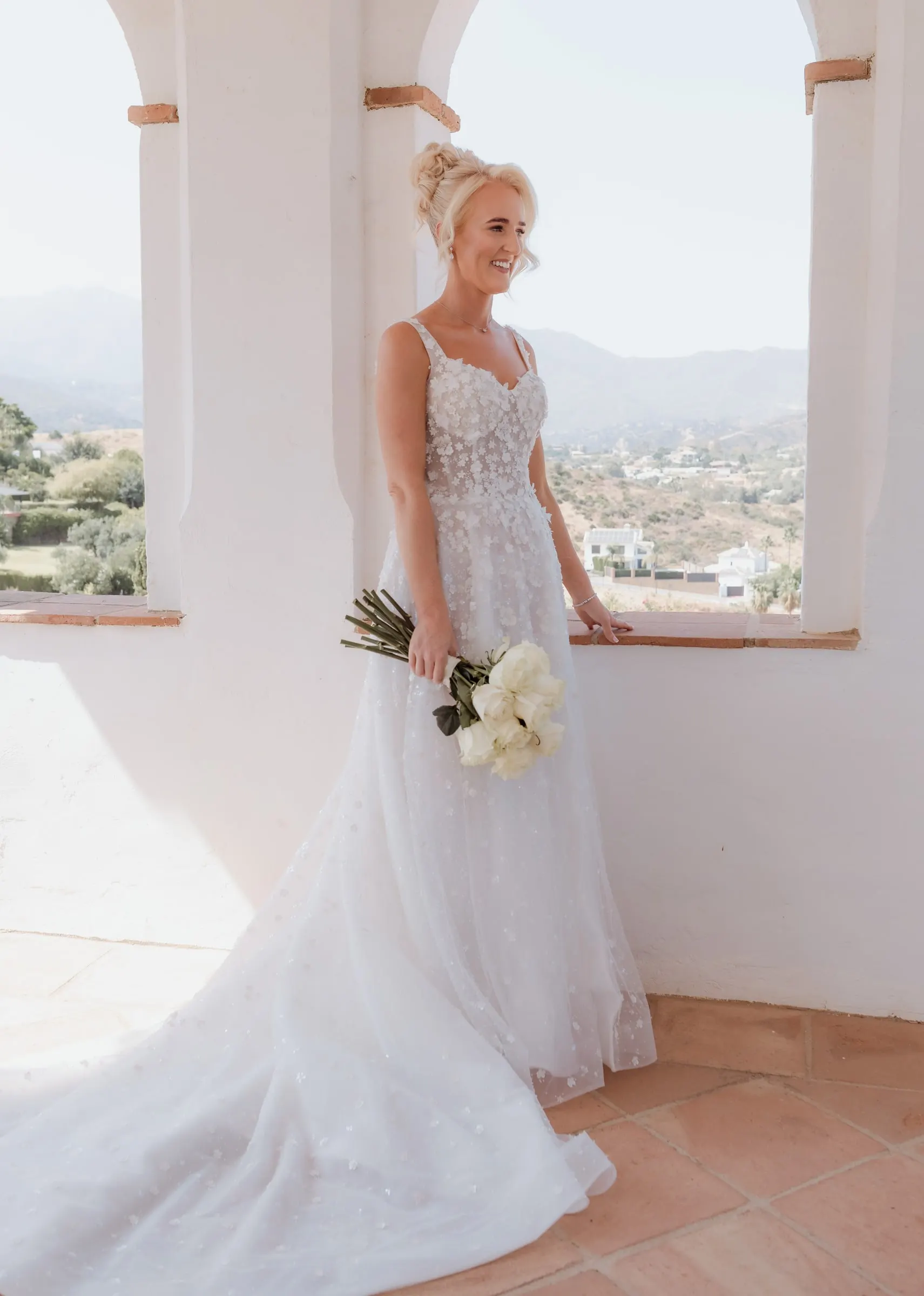 Bride standing in an arched window with the Mijas hills behind