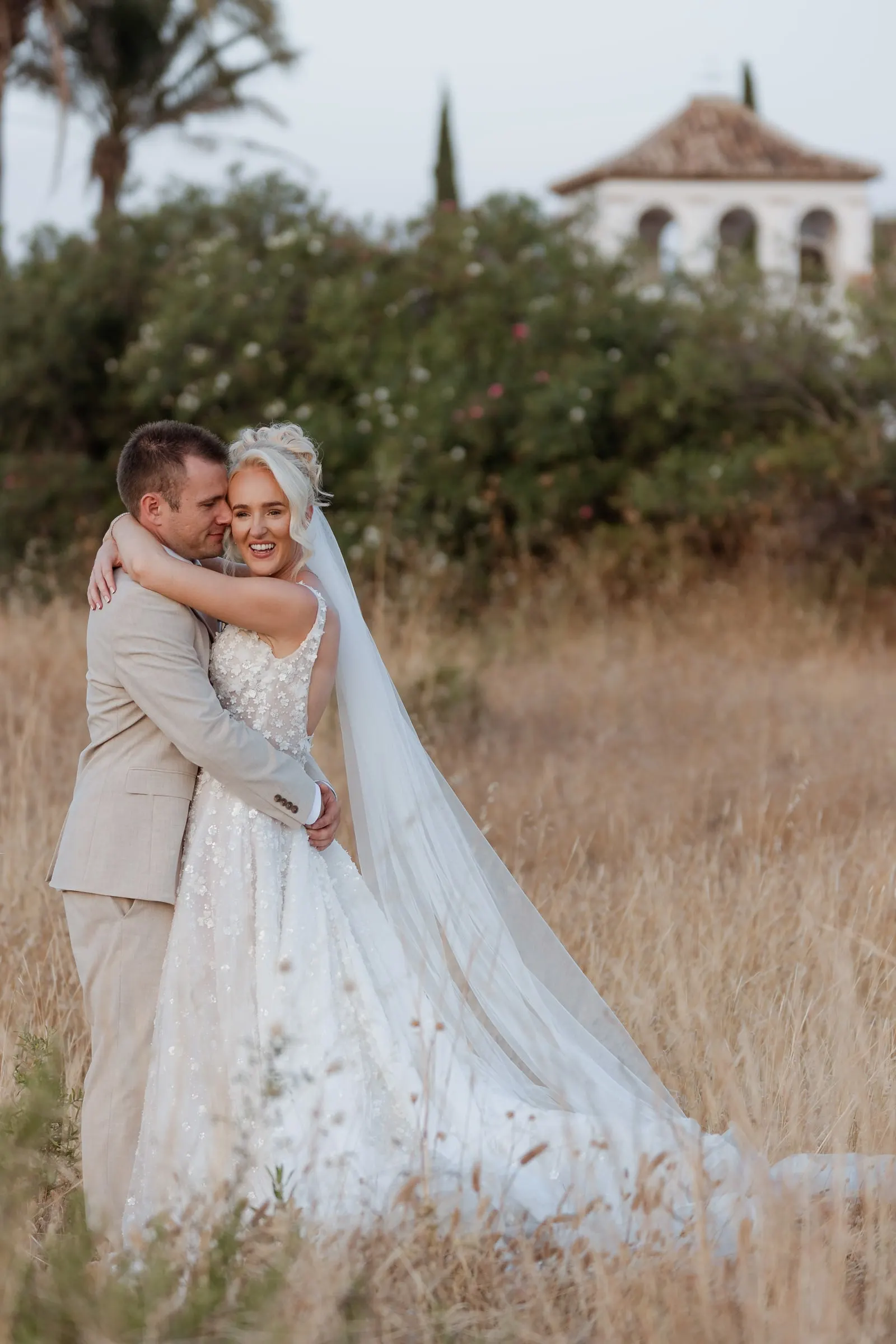 Couple embracing in golden grass with the white tower of Hacienda San José behind