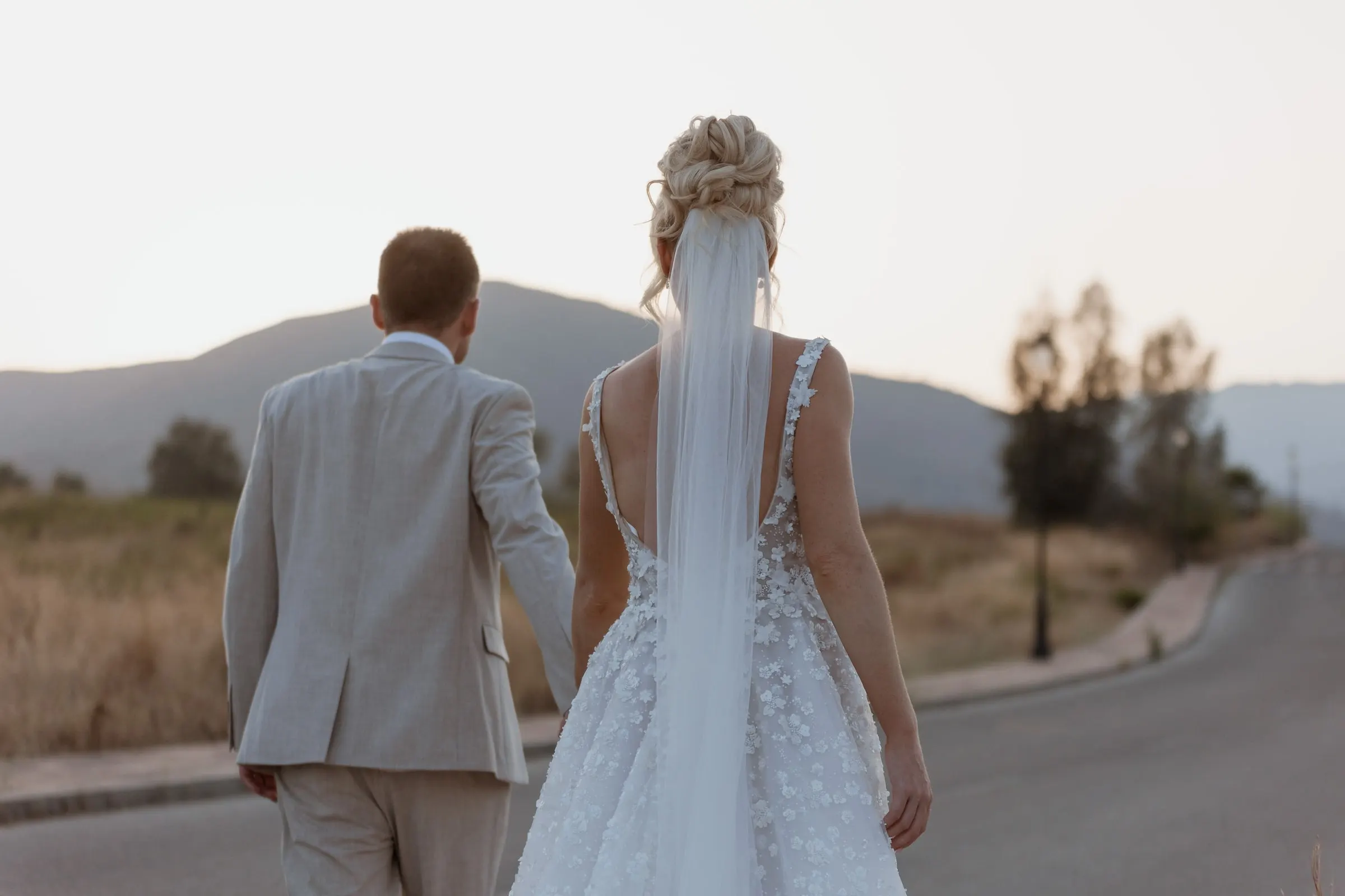 Bride and groom walking along a quiet road towards the hills at sunset