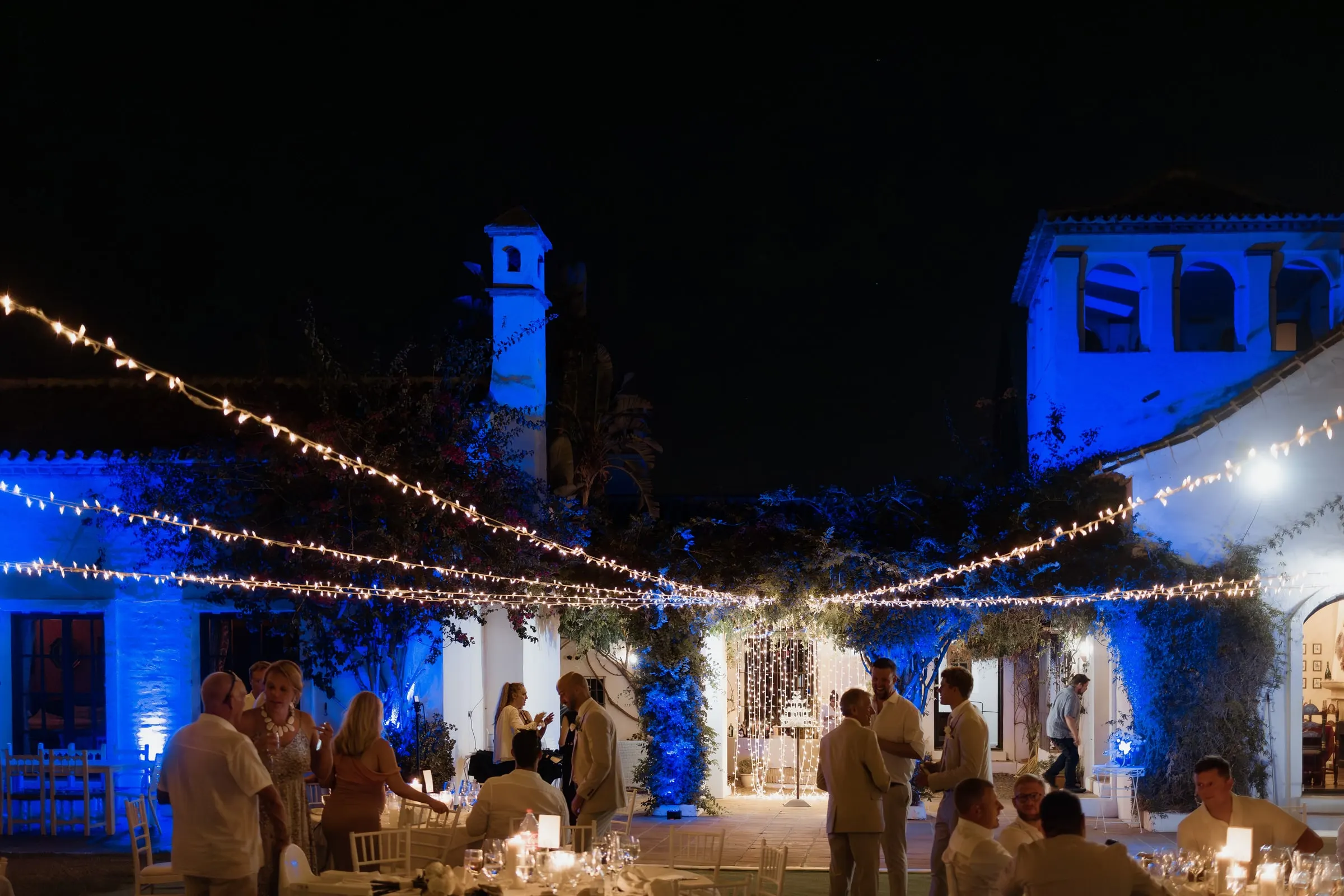 Courtyard at night with blue uplighting, festoon lights and the tower of Hacienda San José
