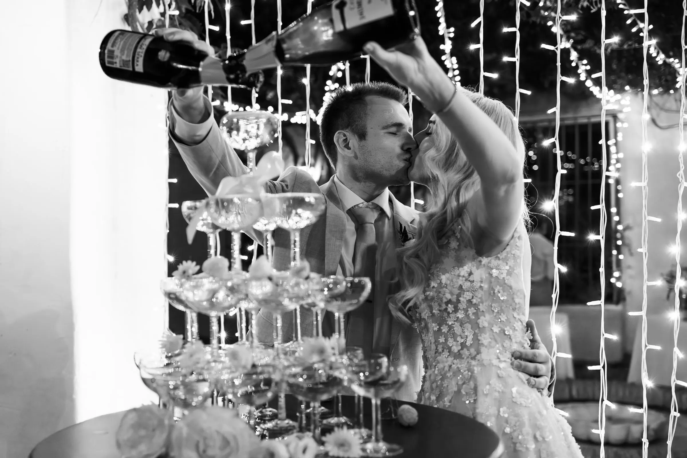 Black and white photo of the couple kissing while pouring the champagne tower