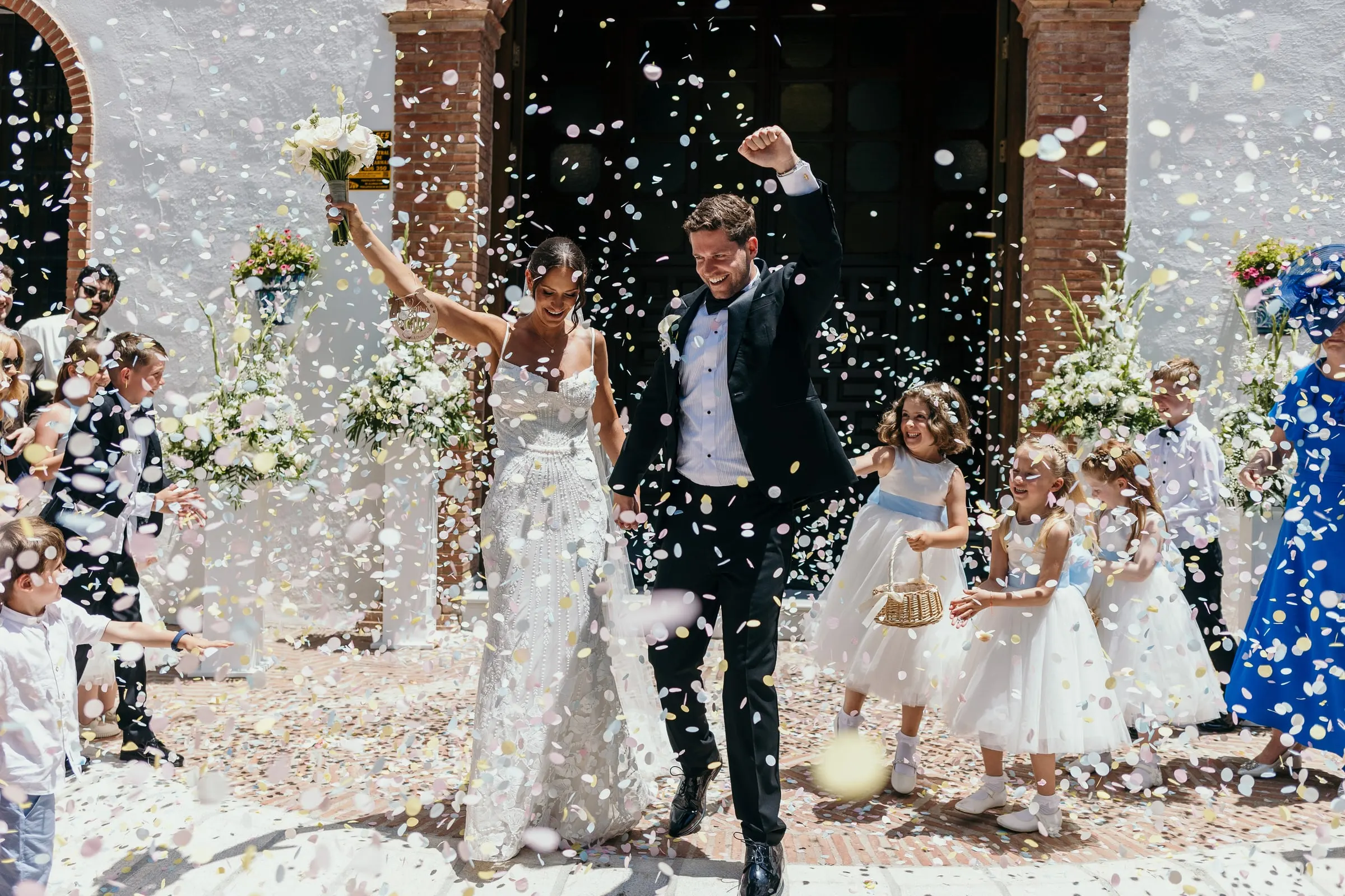 Bride and groom raising their hands as guests throw petals in Mijas Pueblo