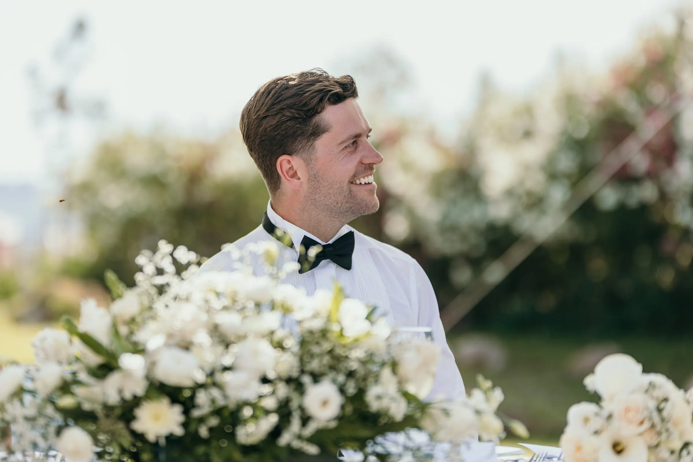Groom laughing behind the white flowers of the top table