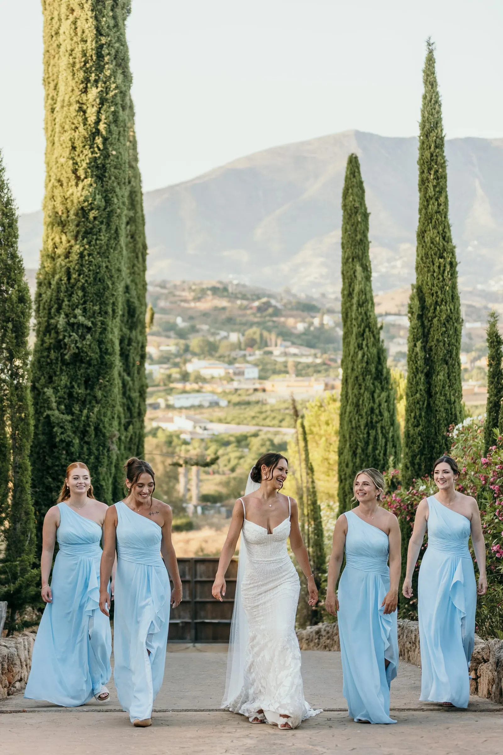 Bride and bridesmaids walking down the cypress avenue at Hacienda San José with the mountains behind