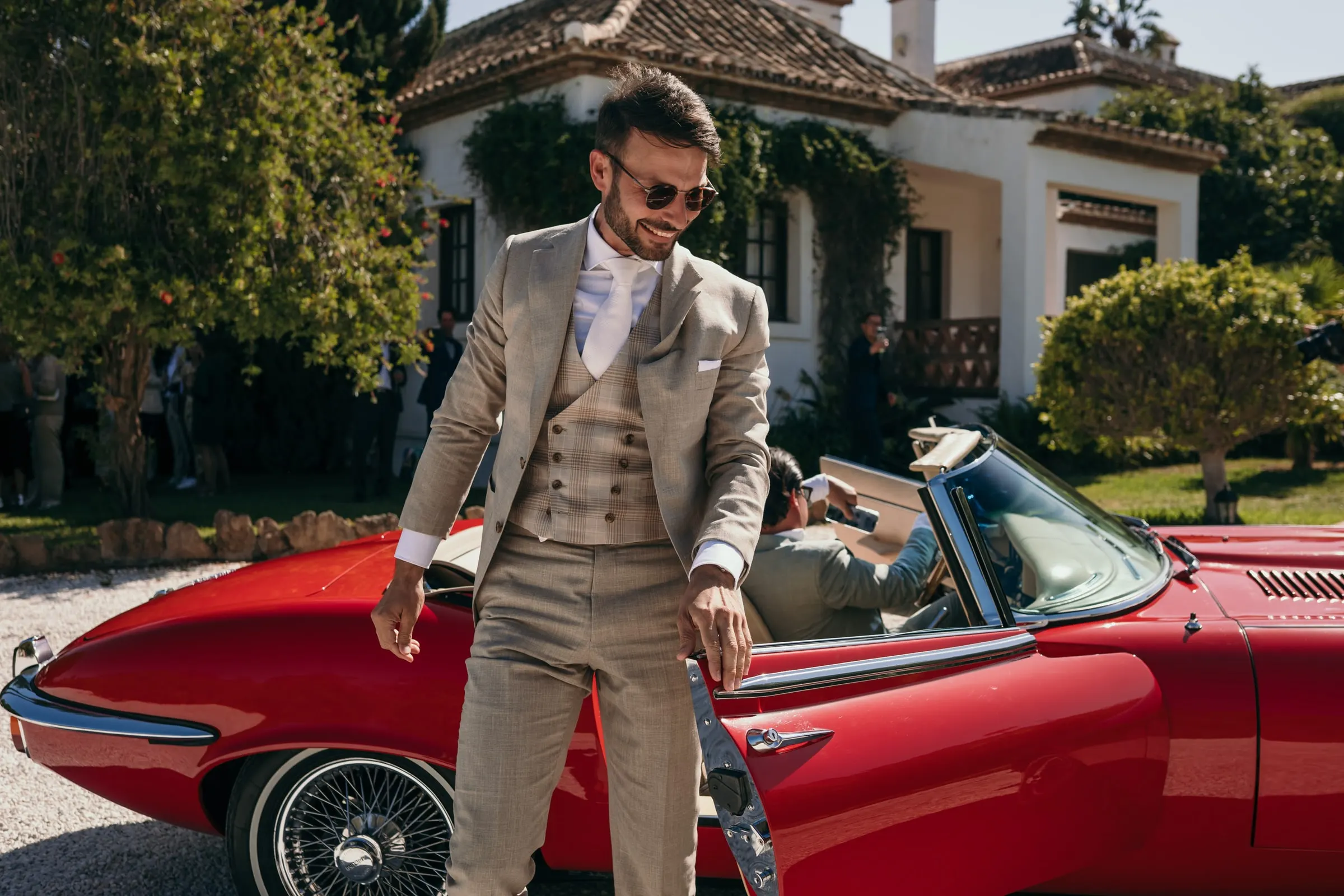 The groom in a beige three-piece suit stepping out of a red vintage convertible, Hacienda San José, Mijas