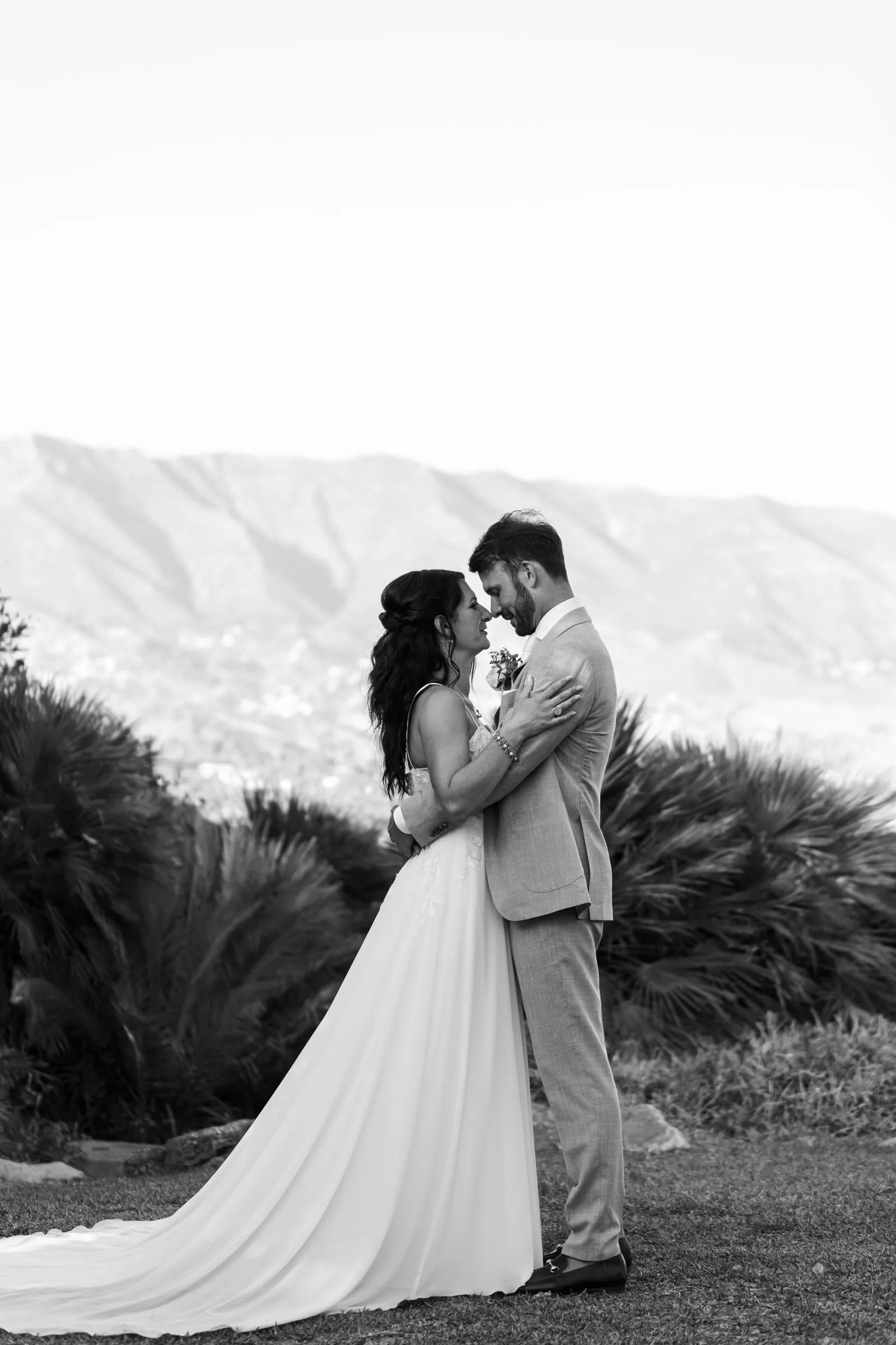 Black and white of the couple embracing on a hillside with the mountains behind, Hacienda San José, Mijas