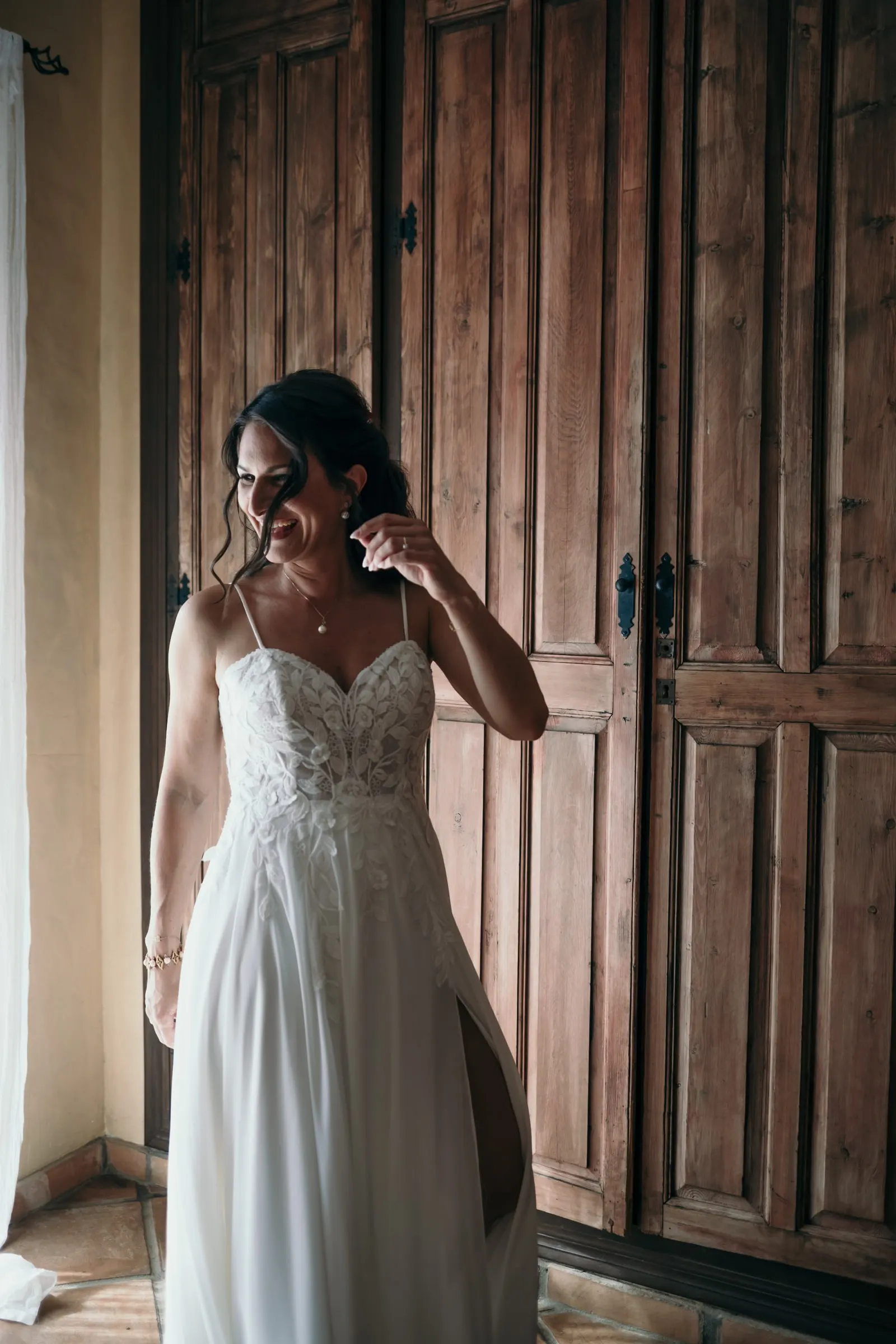 The bride in her lace dress smiling by a tall wooden door as she gets ready, Hacienda San José, Mijas