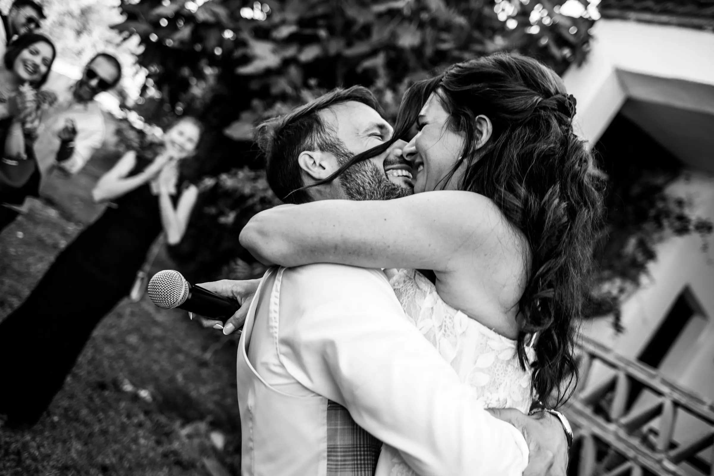 Black and white of the bride and groom hugging tightly as guests laugh around them, Hacienda San José, Mijas