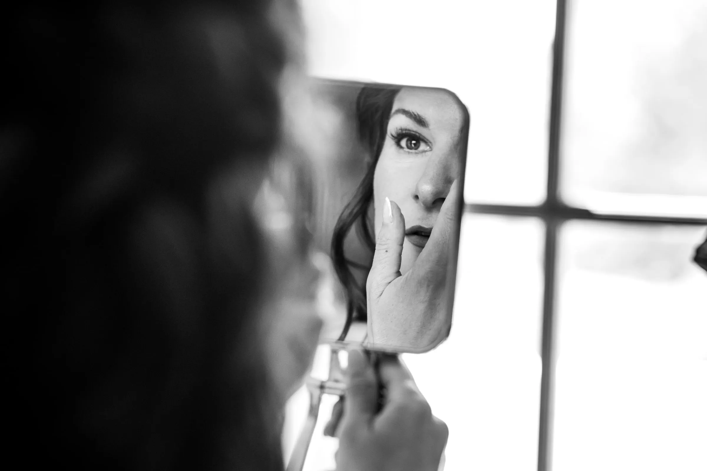 Black and white of the bride checking her make-up in a hand mirror by the window, Hacienda San José, Mijas