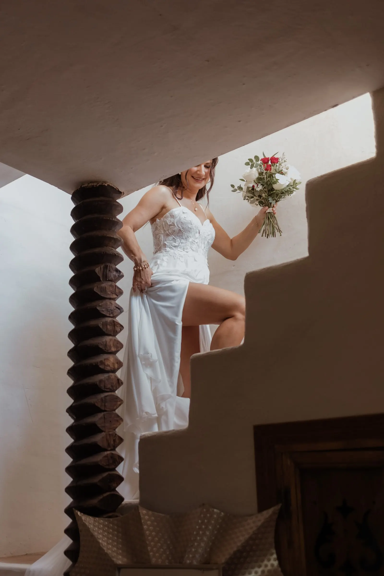 The bride climbing a white staircase with her bouquet, lifting her dress, Hacienda San José, Mijas