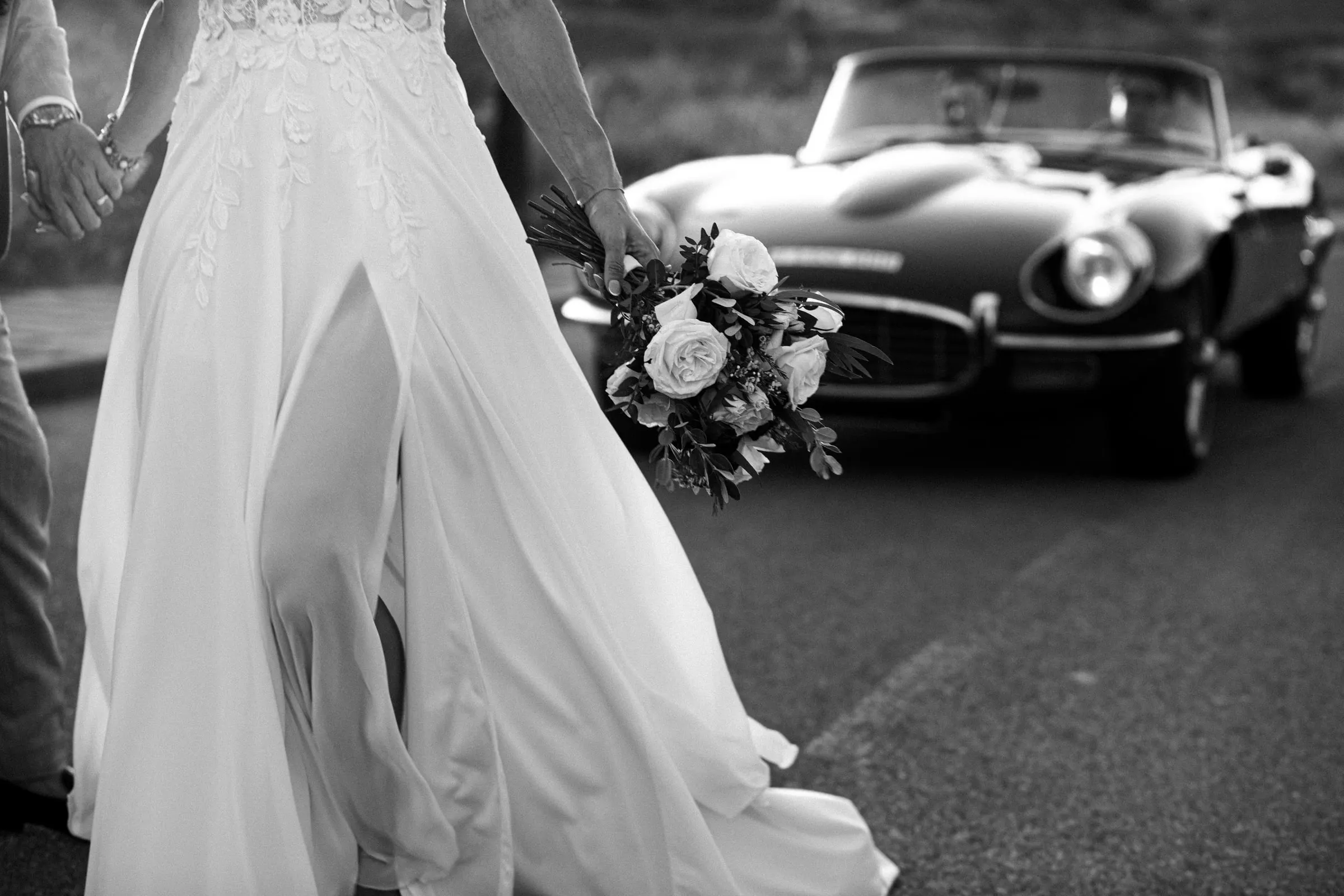 Black and white of the bride's flowing skirt and bouquet beside a vintage convertible, Hacienda San José, Mijas