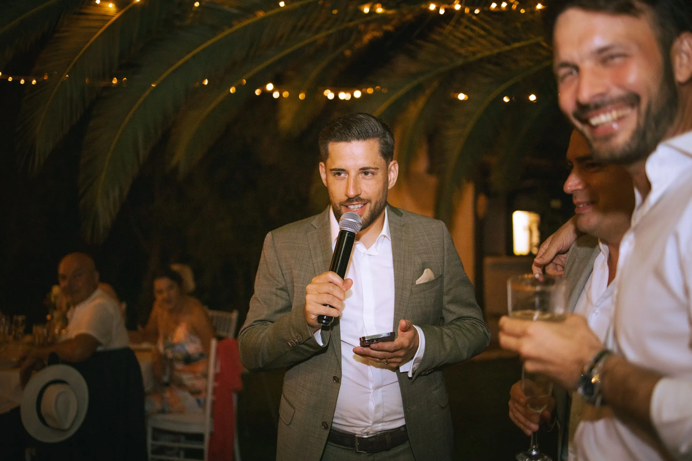 A guest with a microphone giving a toast under palm trees and fairy lights, Hacienda San José, Mijas