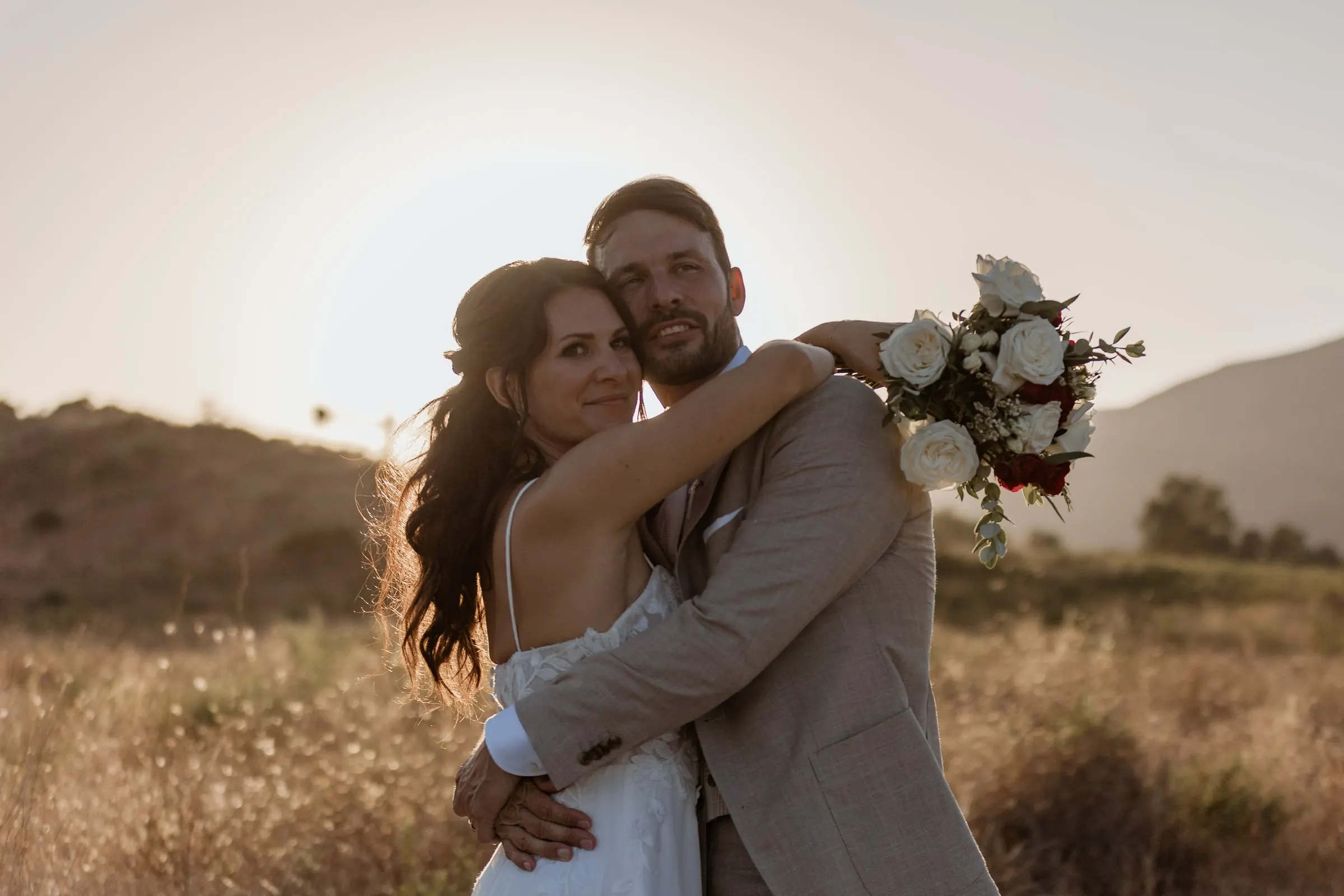The couple hugging and smiling at the camera in a dry field at sunset, Hacienda San José, Mijas