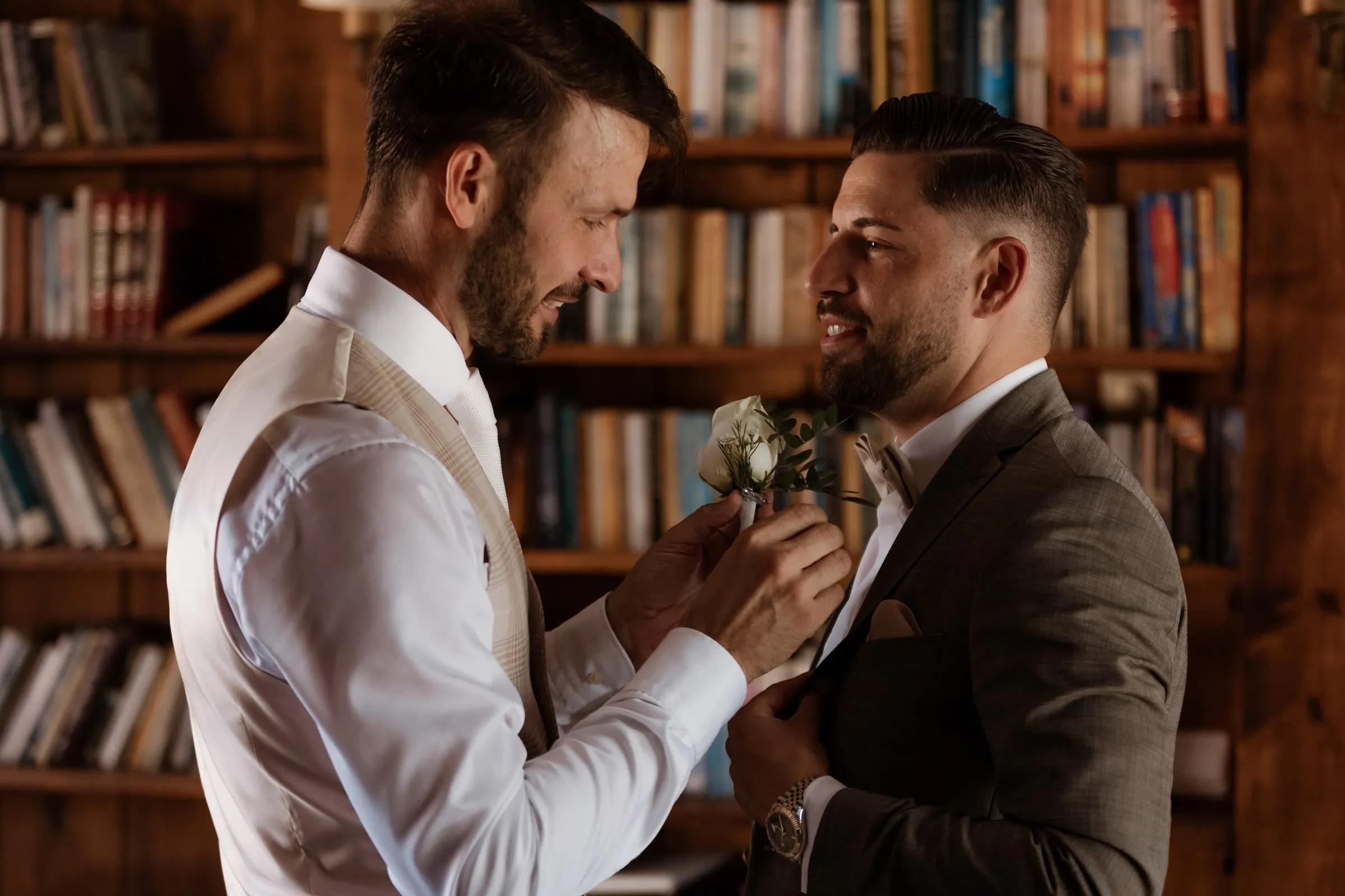The groom pinning a buttonhole on a friend's jacket in a wood-panelled library, Hacienda San José, Mijas
