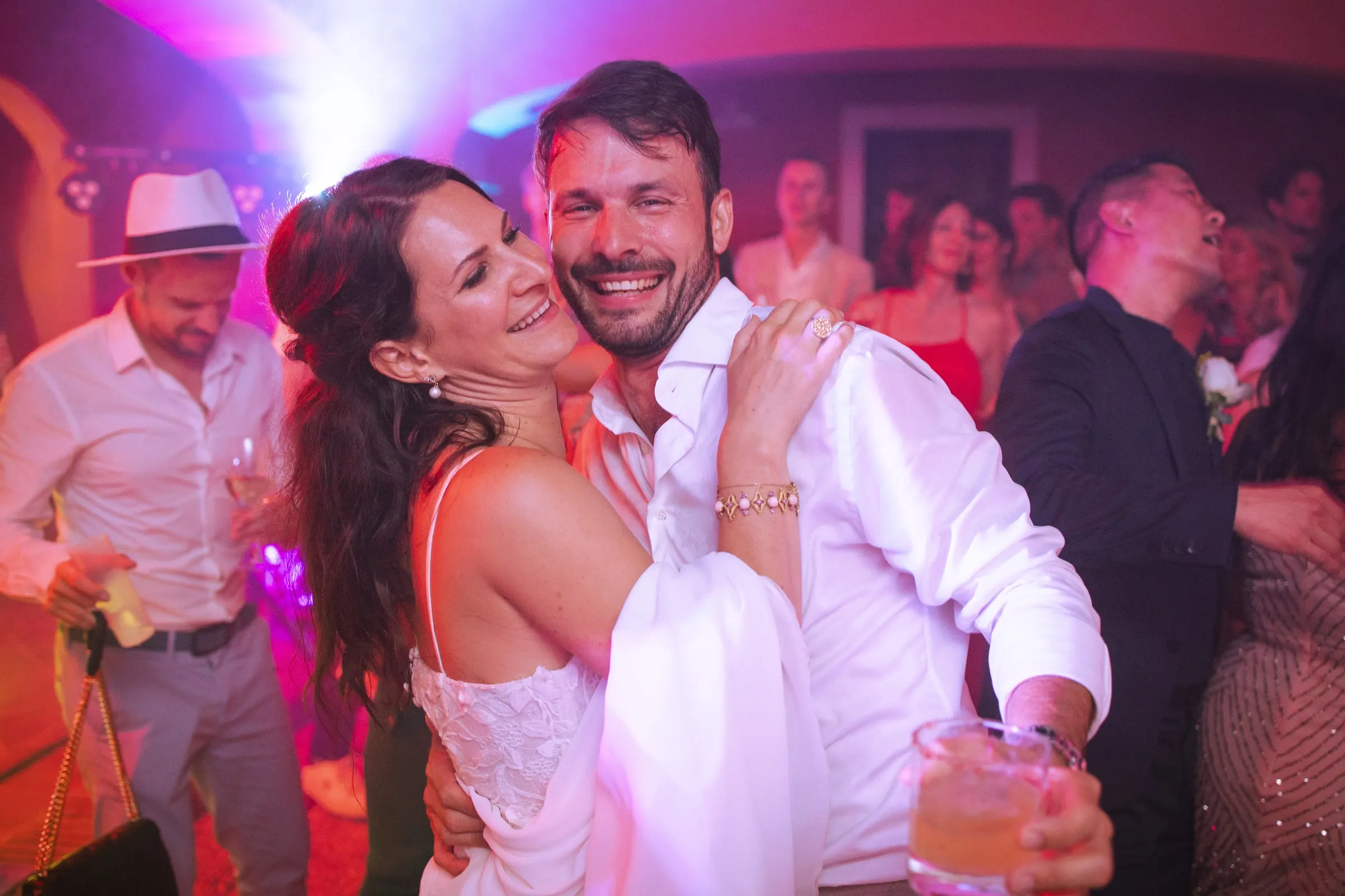 Bride and groom hugging and grinning on the dance floor under pink party lights, Hacienda San José, Mijas