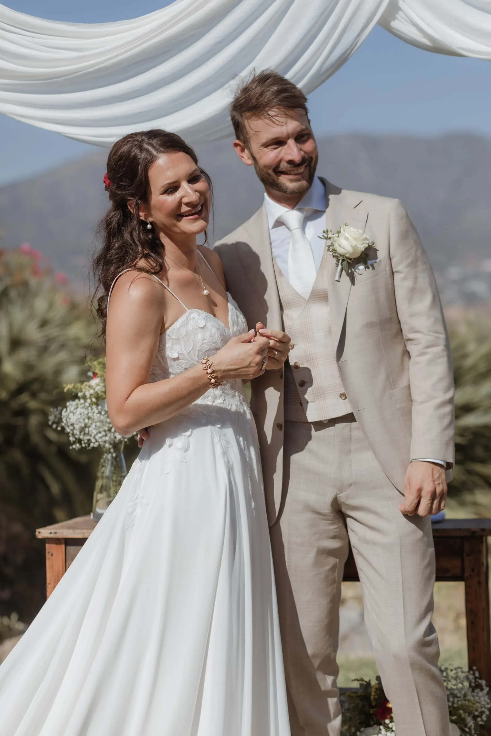 Bride and groom laughing side by side at the ceremony table, mountains behind, Hacienda San José, Mijas