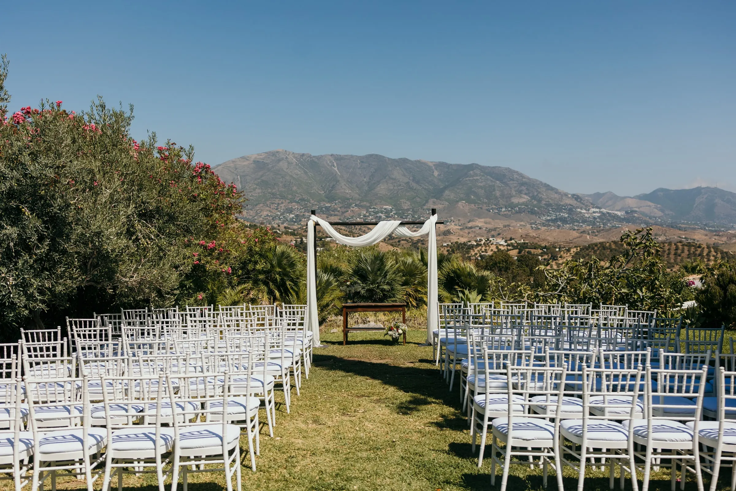Rows of white chairs facing a draped canopy with the Mijas mountains beyond, Hacienda San José, Mijas