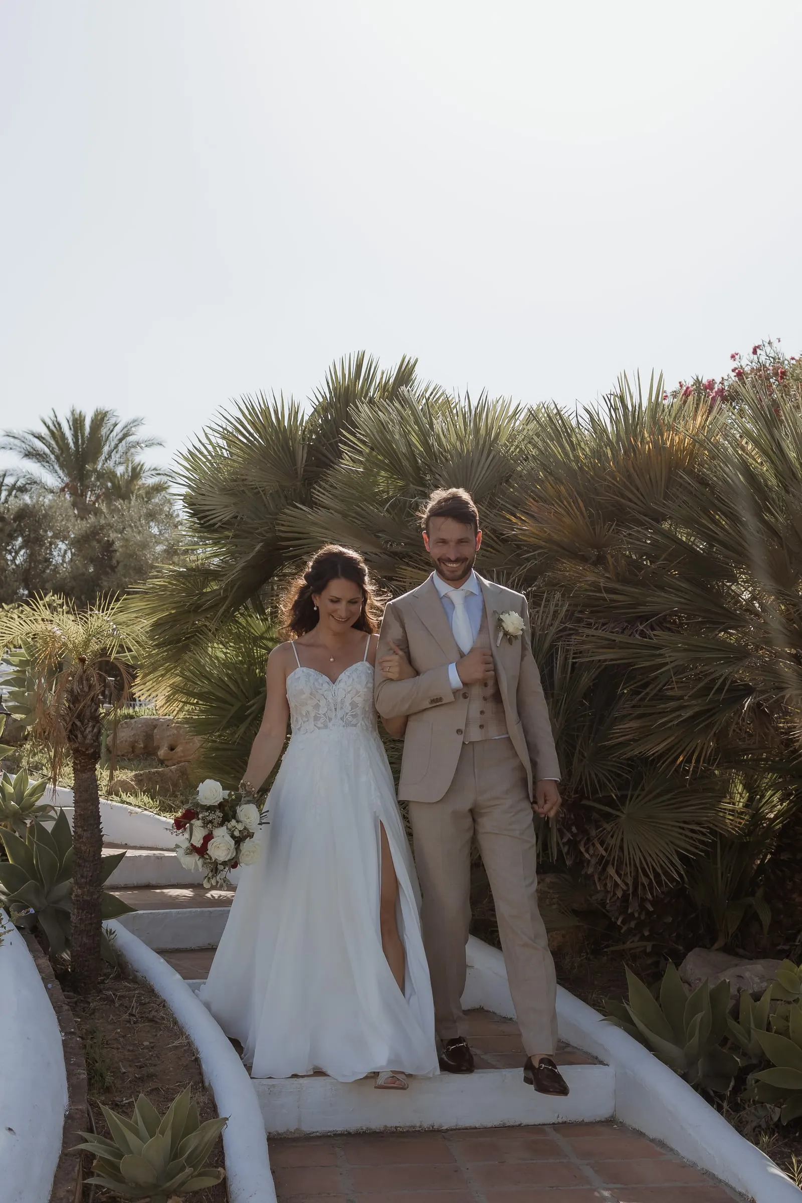 Bride and groom walking hand in hand down whitewashed steps among palm trees, Hacienda San José, Mijas