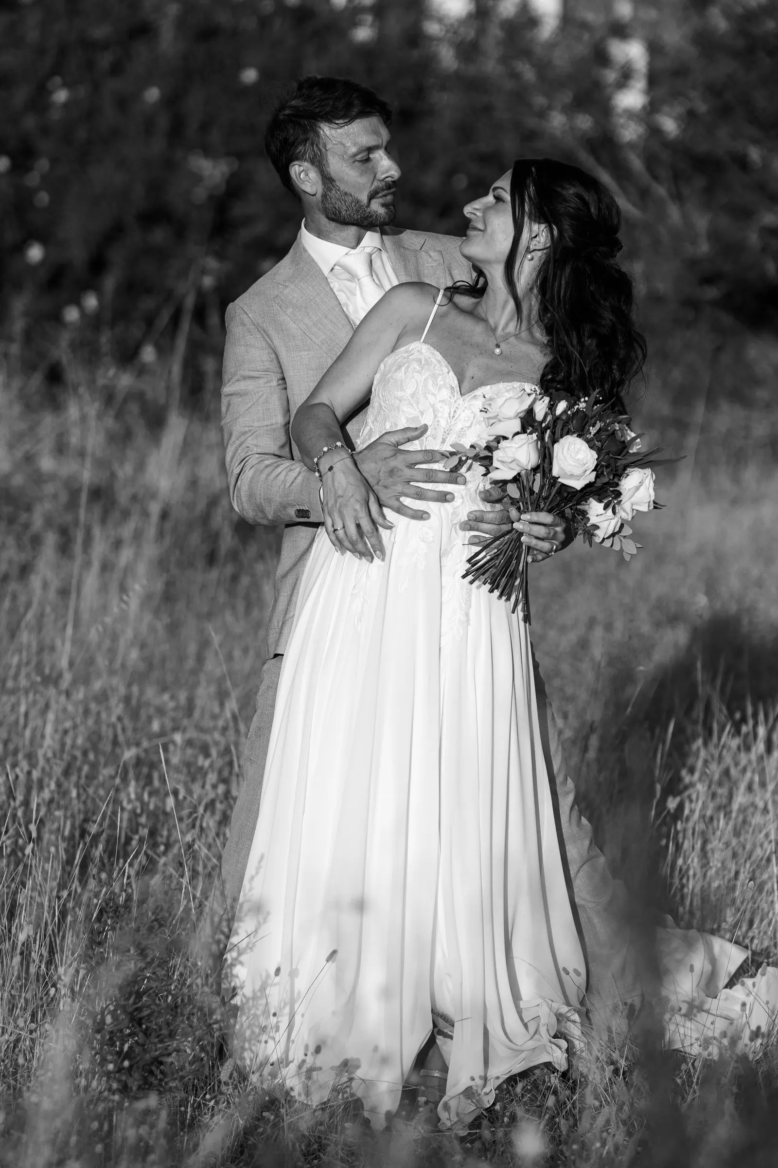 Black and white of the groom holding the bride from behind in tall grass, Hacienda San José, Mijas