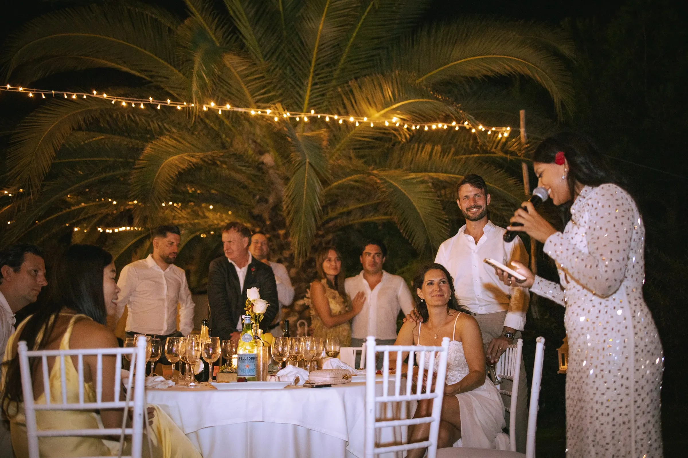 A guest in a sequinned dress giving a speech at night as the table listens, Hacienda San José, Mijas